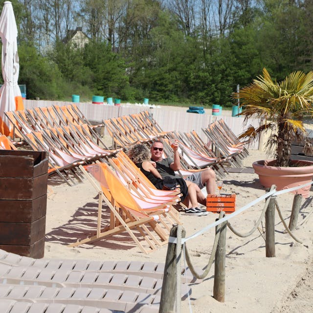 Eine Reihe von Liegestühlen am Sandstrand des Otto-Maigler-Sees. Zwei Besucher genießen schon die Sonne.