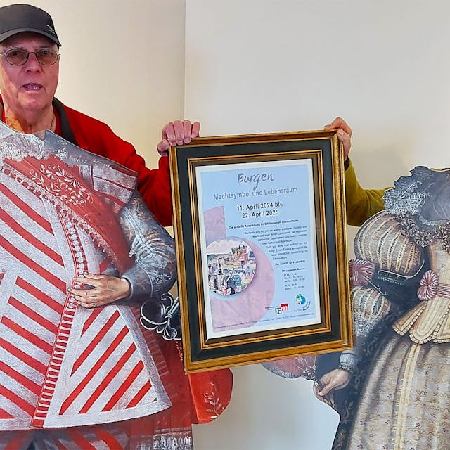 Wolfgang Doppelfeld und Dr. Ruth Kirstgen stehen hinter zwei Pappaufstellern mit historischen Kostümen.