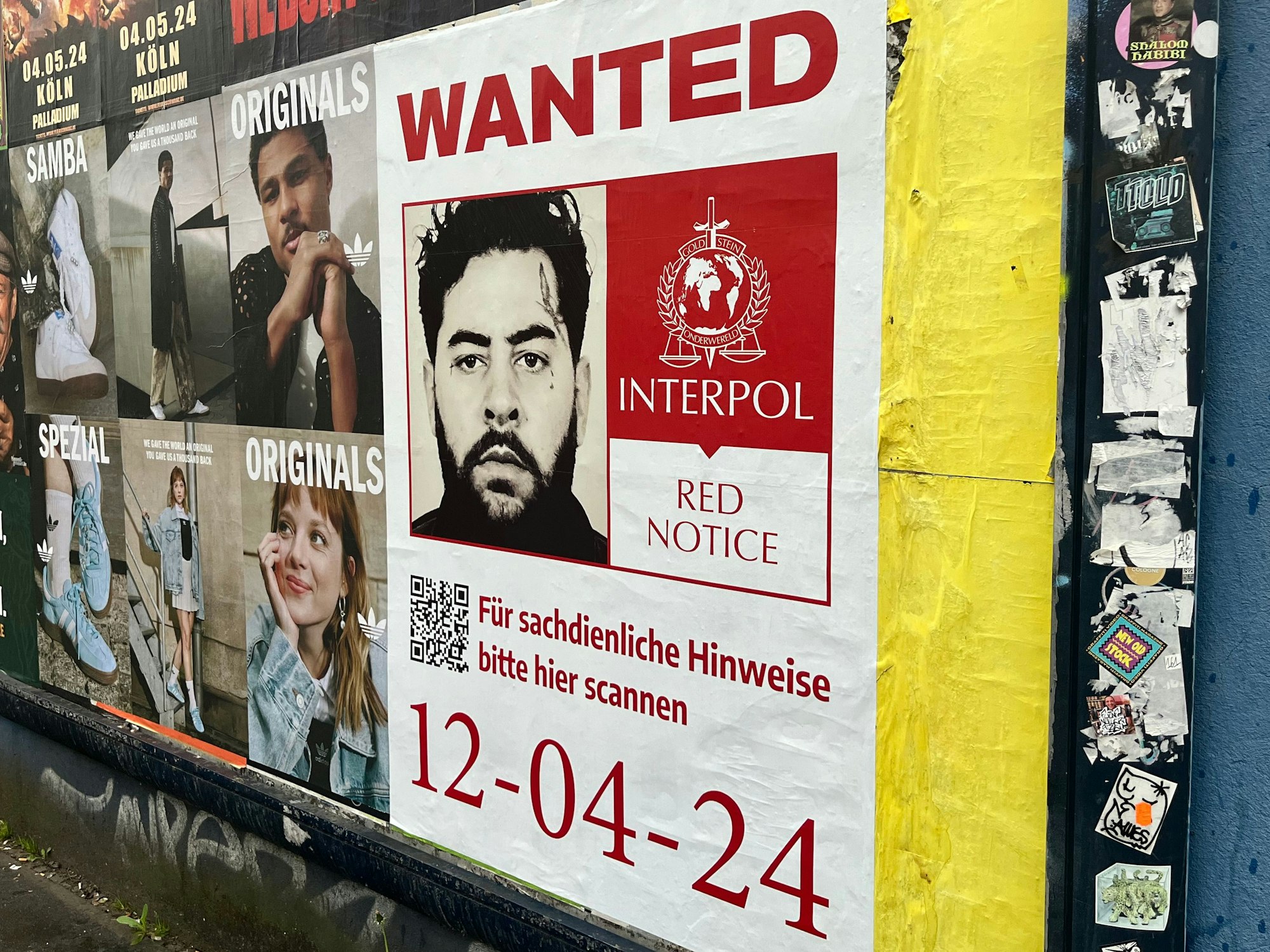 Ein Plakat hängt an der Wand. Darauf steht „Wanted“ und Interpol.