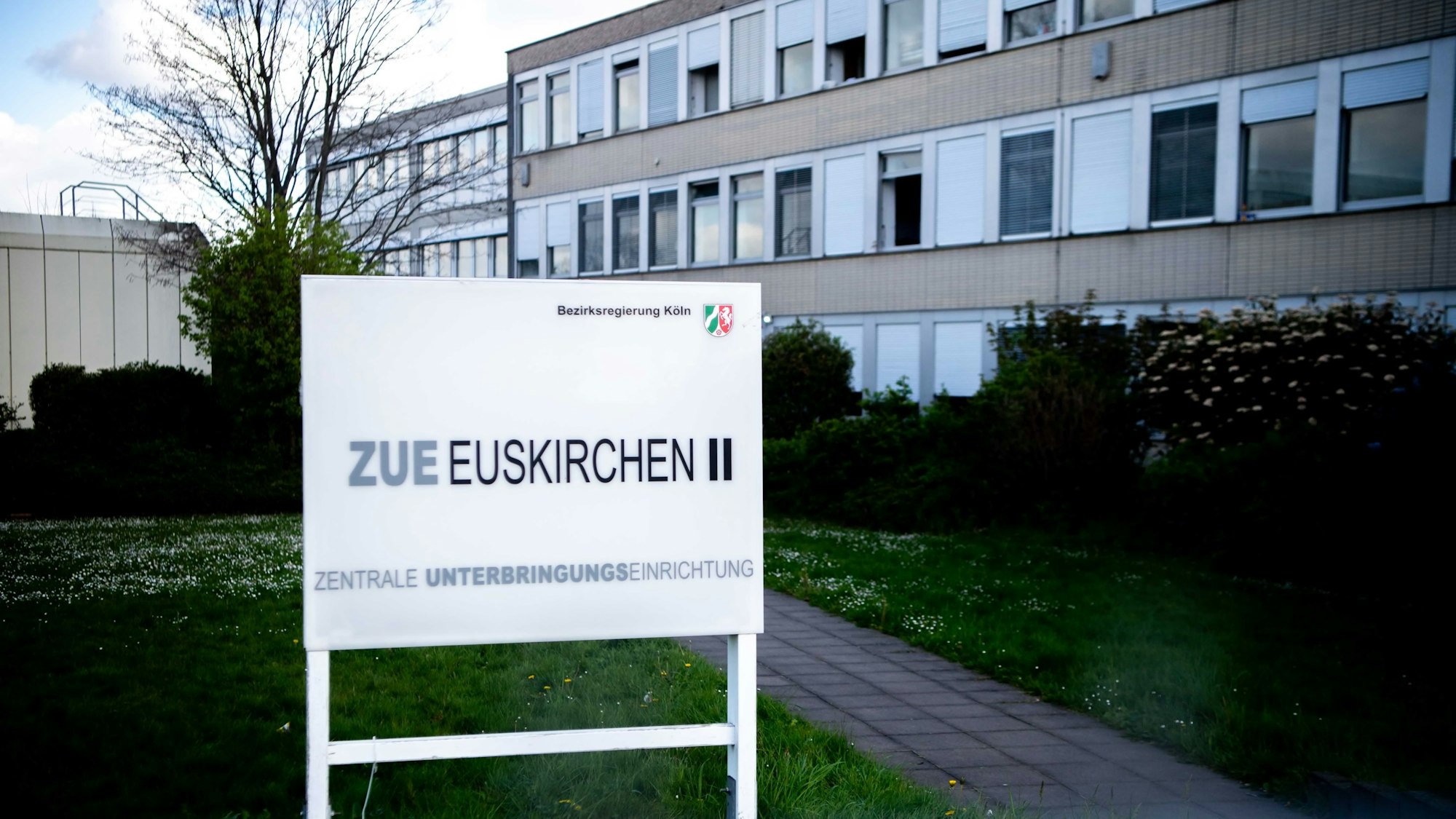 Das Bild zeigt ein Hinweisschild für die ZUE in Euskirchen. Im Hintergrund ist ein Teil des Gebäudes zu erkennen.