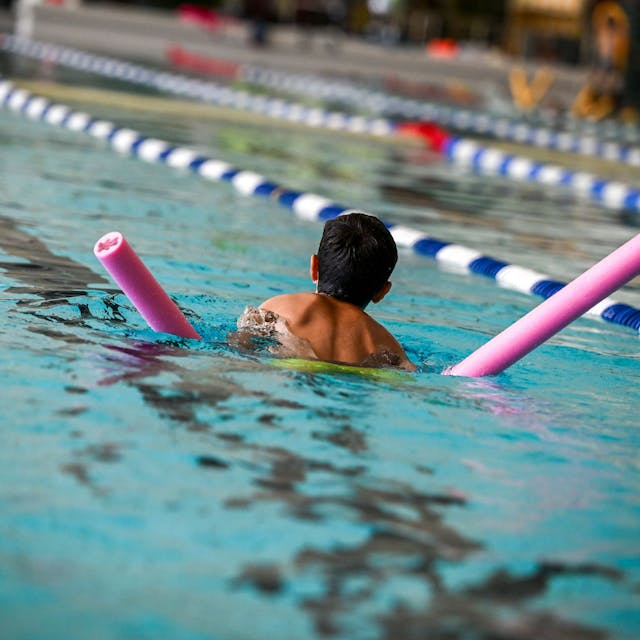 Ein Kind schwimmt mit Schwimmnudel durch ein Becken.