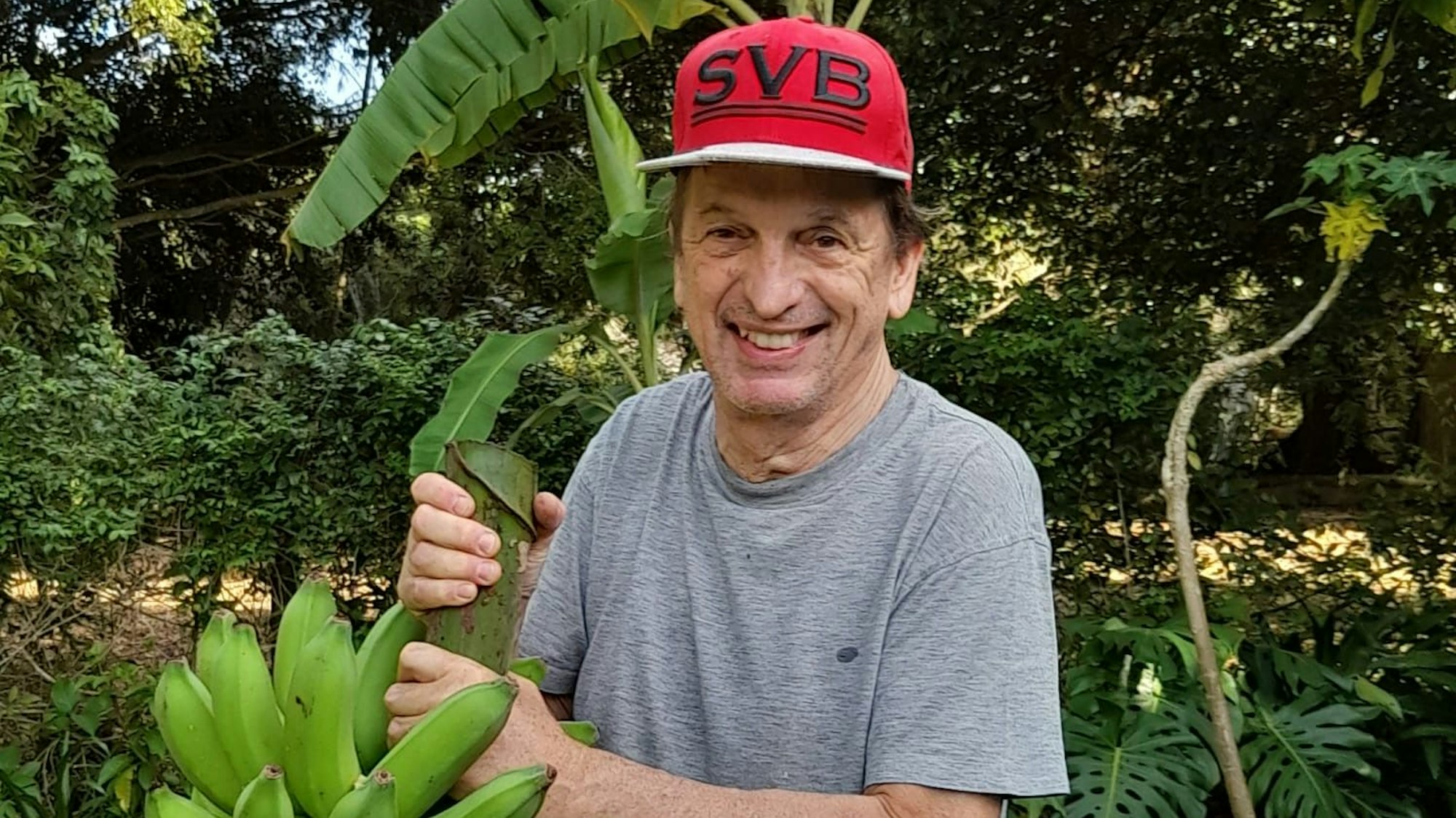 Der Bayer-04-Fan Klaus Gottschalk lebt in Nordaustralien, hier erntet er Bananen im Garten mit seiner Fußball-Kappe auf dem Kopf.