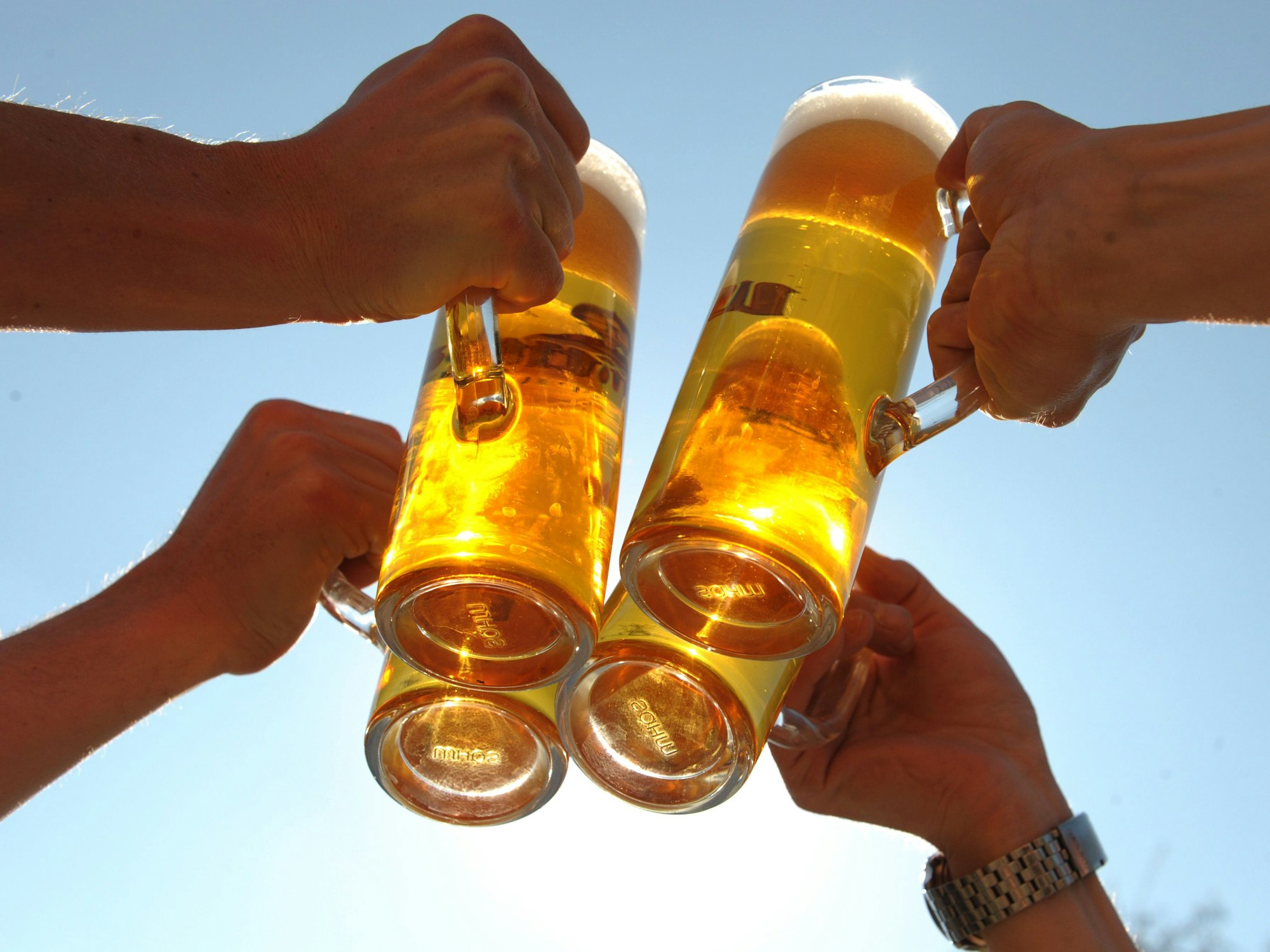 Vier Menschen stoßen mit gläsernen Bierkrügen an