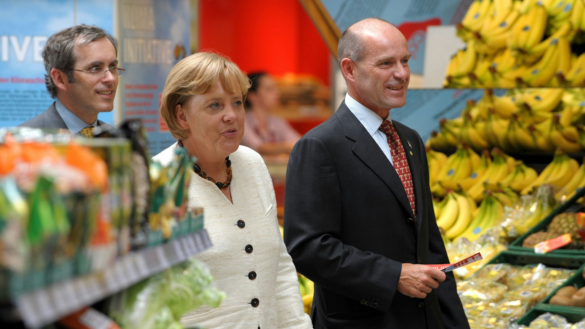 Angela Merkel geht mit Karl-Erivan Haub und Christian Haub durch einen Supermarkt.