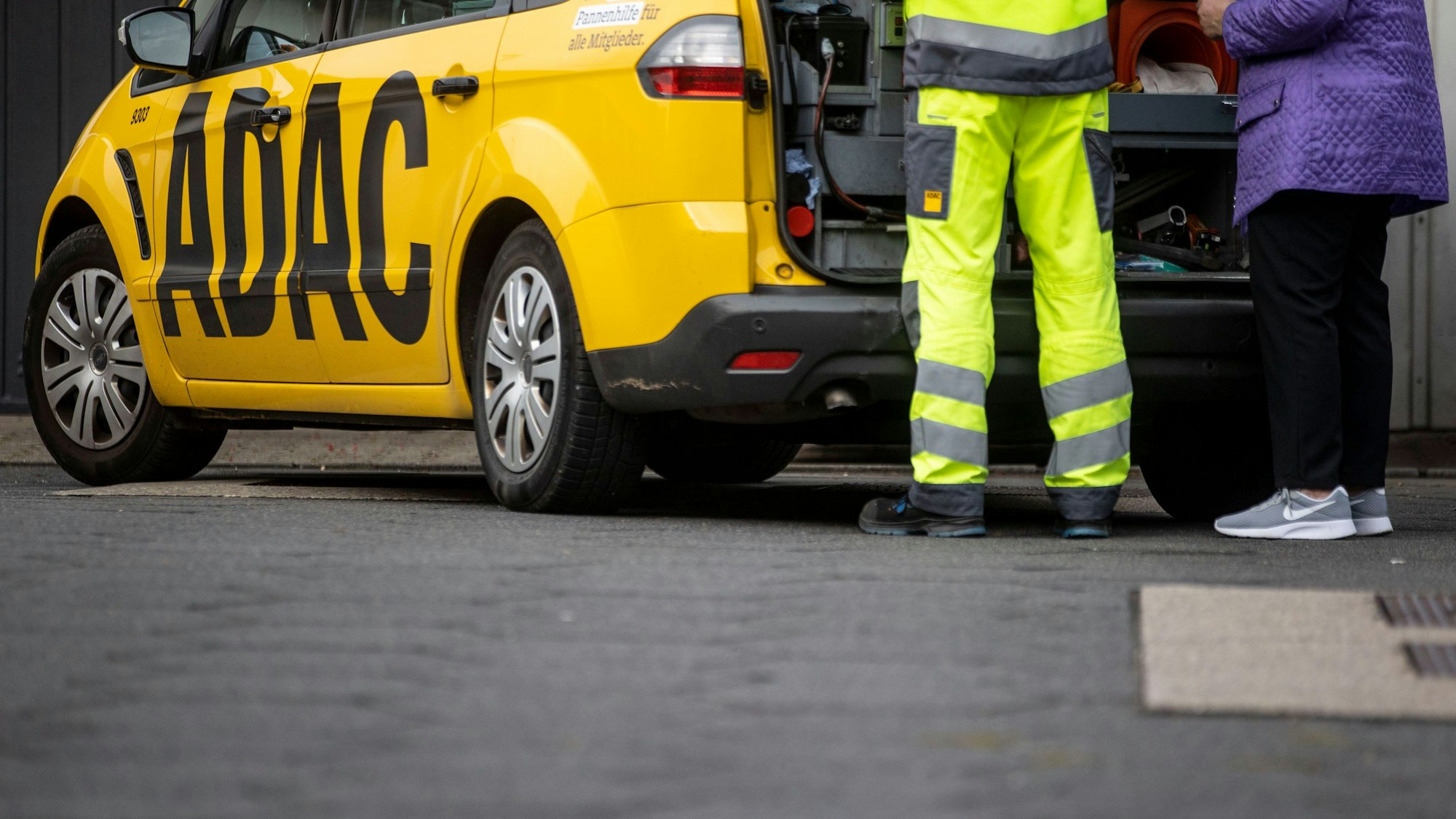 Ein Mitarbeiter des ADAC steht mit seinem gelben Fahrzeug an einer Straße in Duisburg und hilft einer Frau.