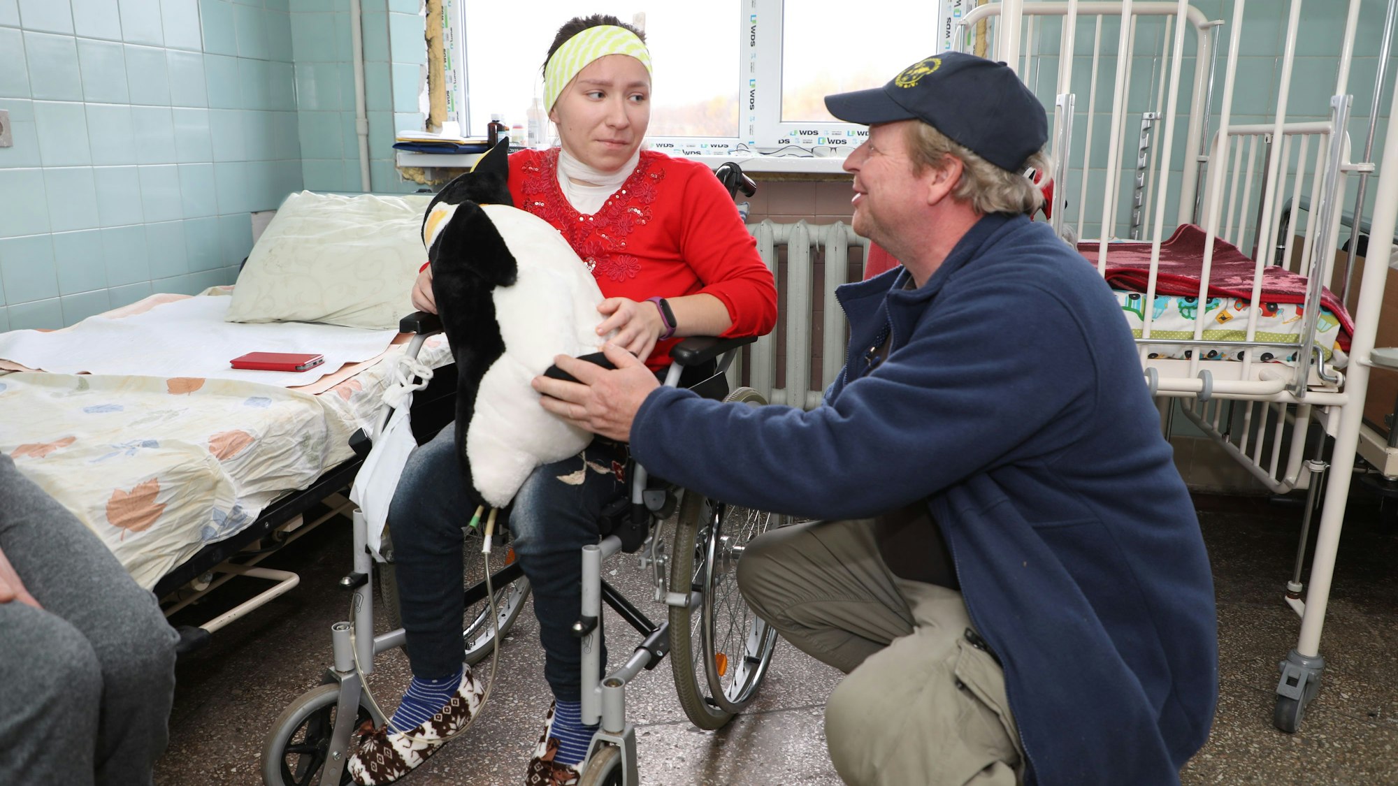 Ein Mitarbeiter der Humanitären Hilfe Bergisch Gladbach übergibt einem Mädchen in einem Rollstuhl im Kinderkrankenhaus von Lviv/Ukraine einen Stoffpinguin.