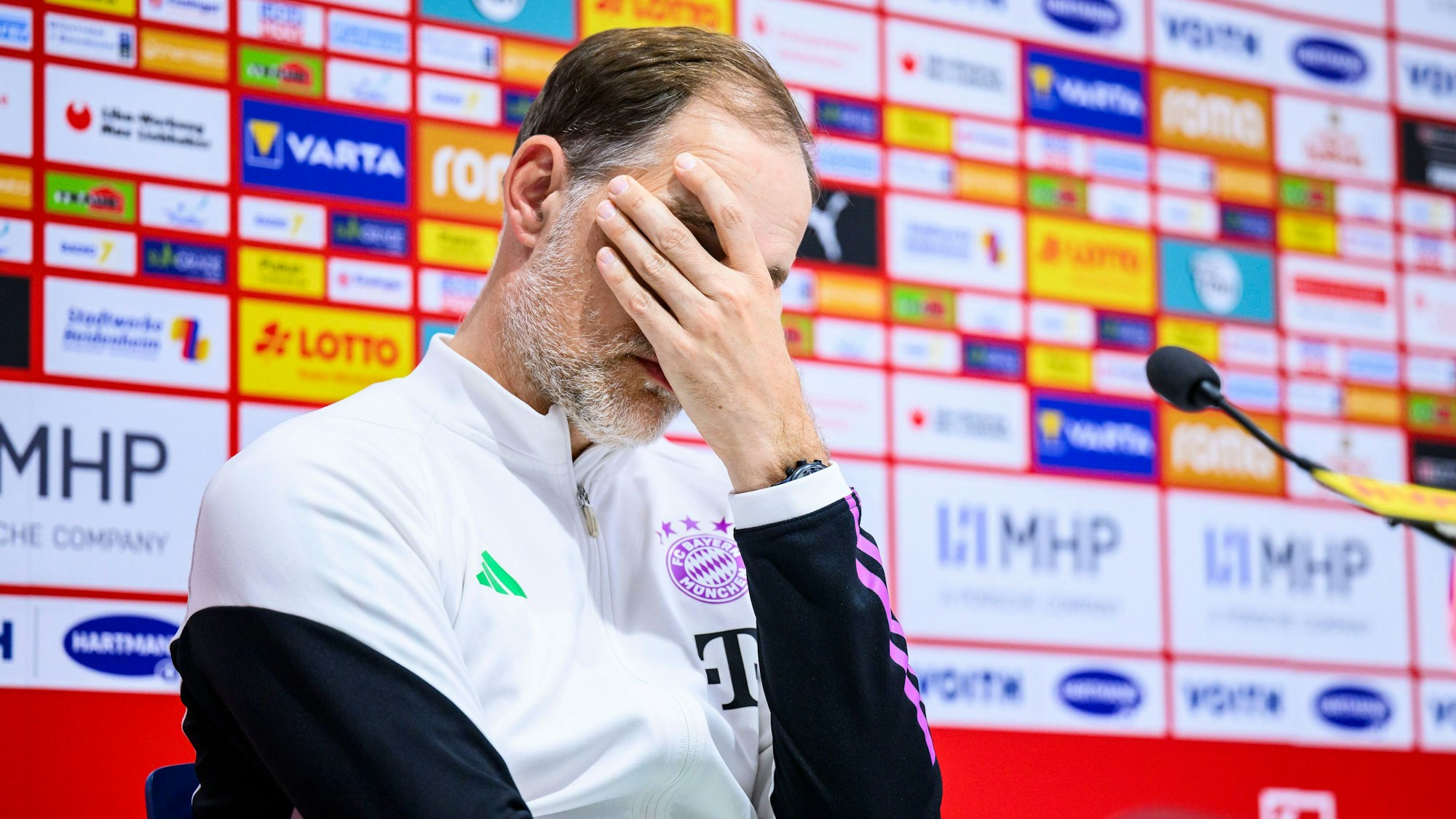 Trainer Thomas Tuchel vom FC Bayern München reagiert nach dem Spiel auf der Pressekonferenz und hält sich die Hand vors Gesicht.