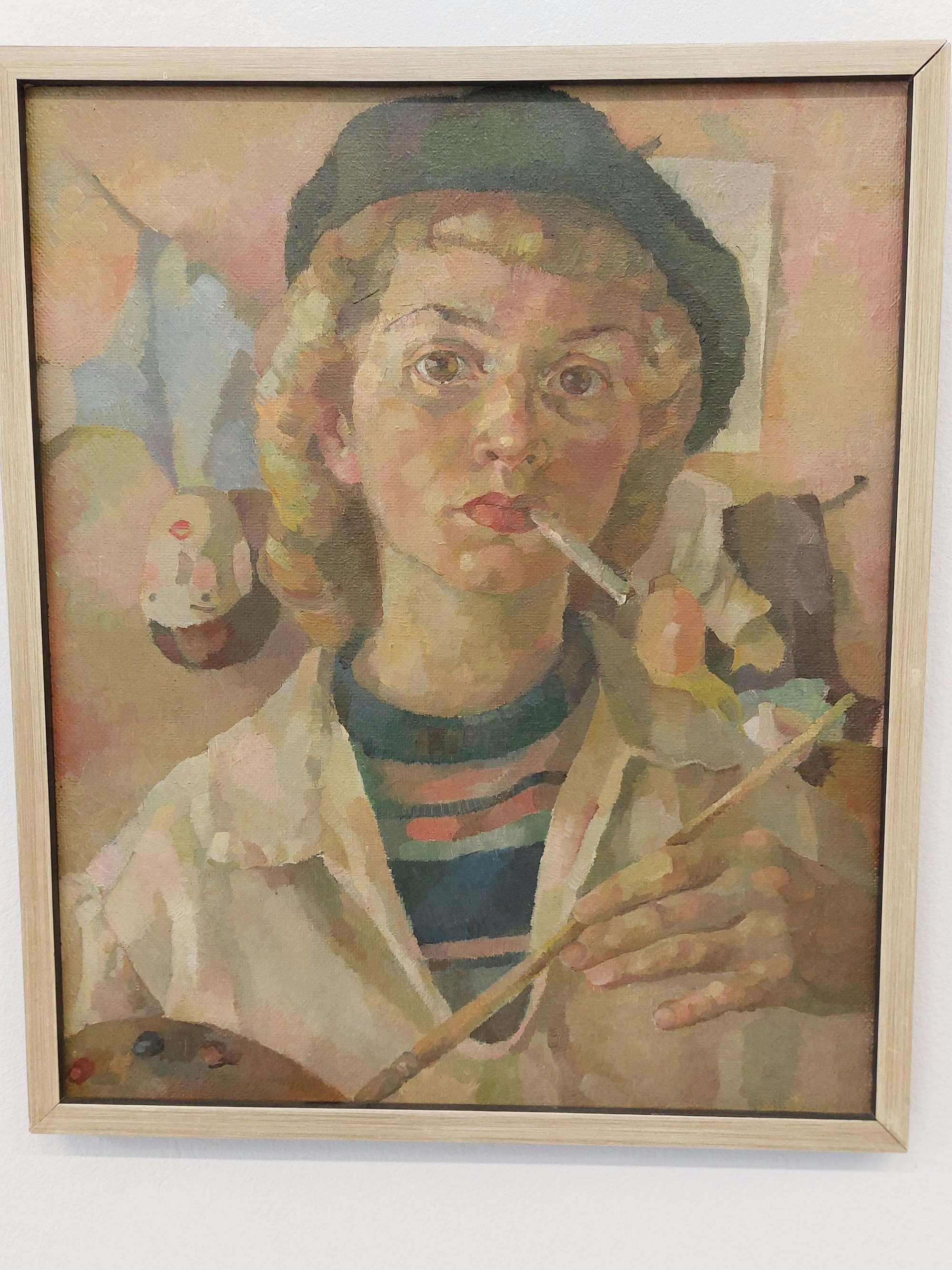 Das Porträt einer jungen Frau; sie zeigt sich mit Baskenmütze, Pinsel und Zigarette im Mundwinkel als Künstlerin.
