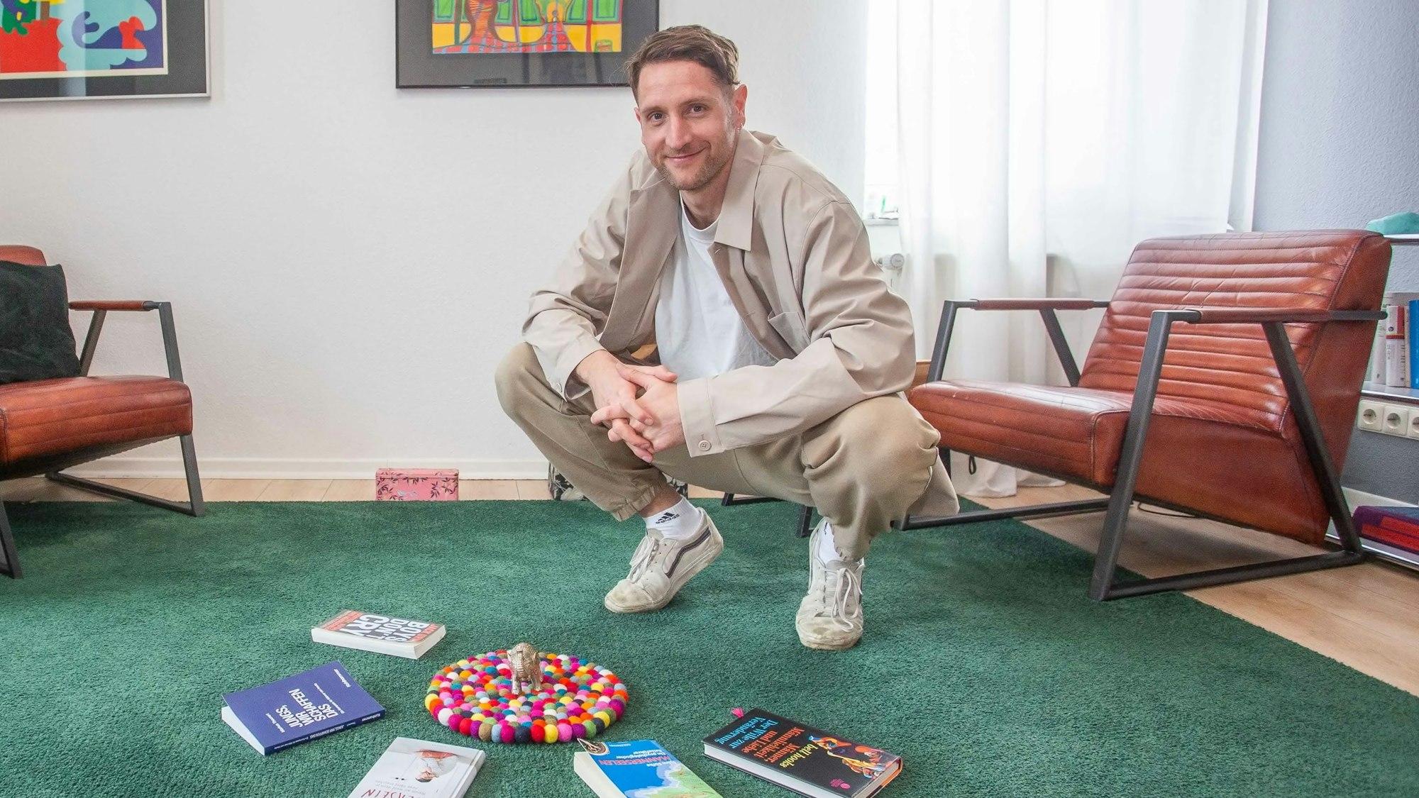 Therapeut Matthias Stinn in der Hocke auf einem grünen Teppich, vor sich hat er Bücher liegen.