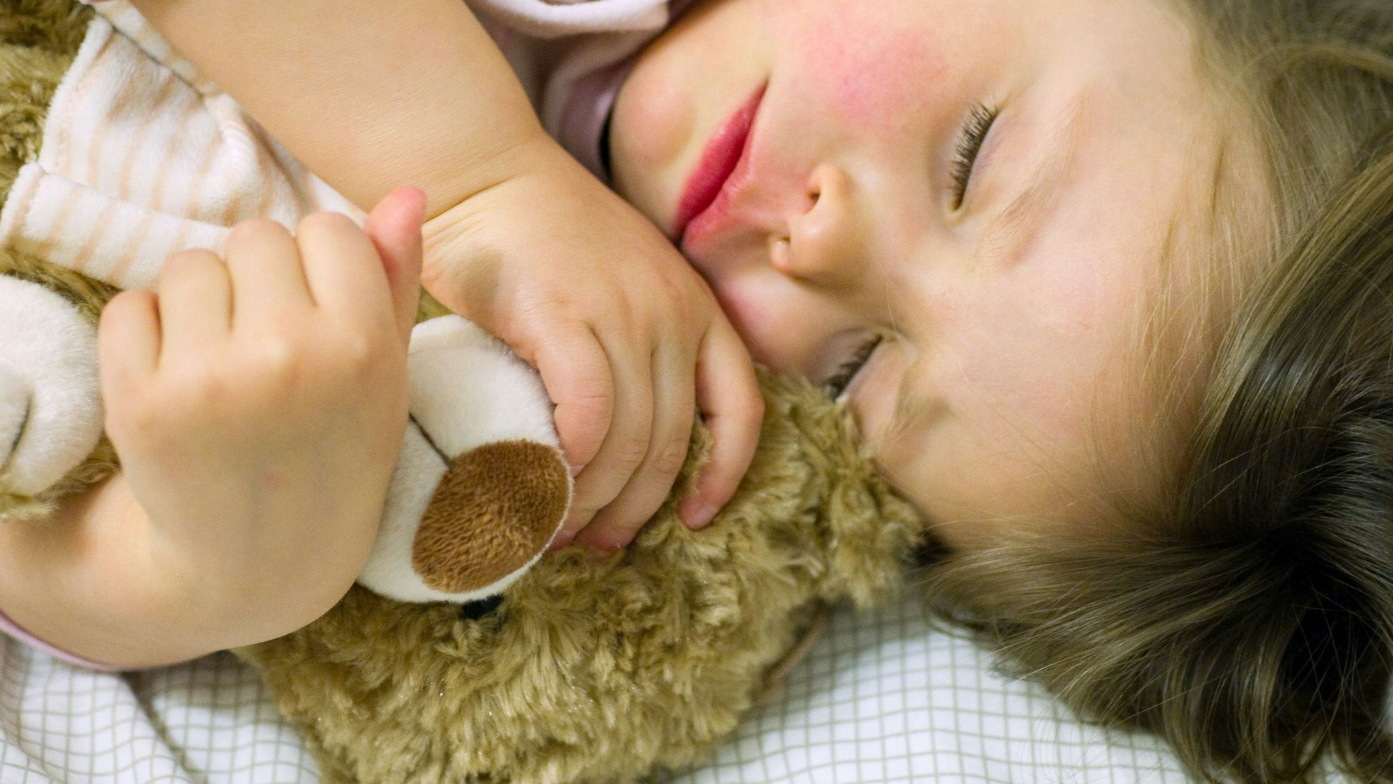 Ein Mädchen schläft mit ihrem Teddy im Arm.