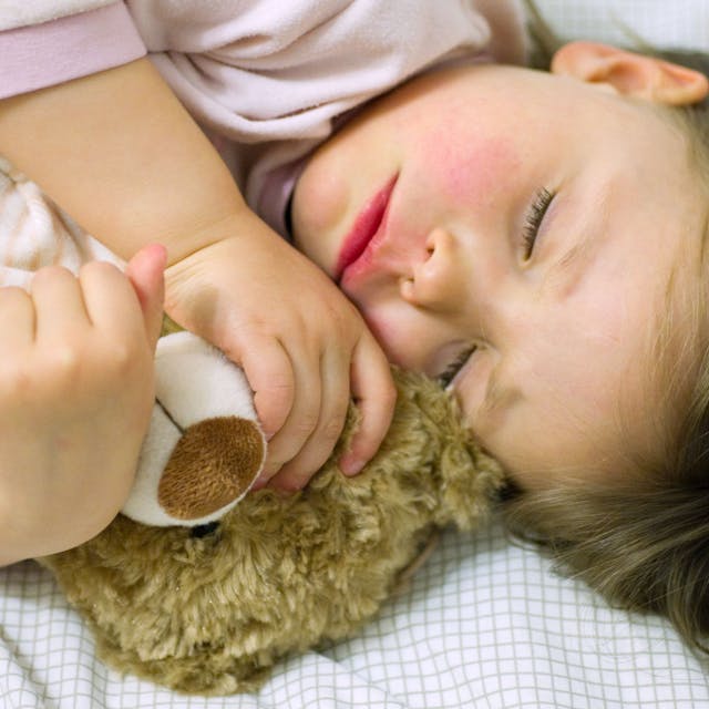 Ein Mädchen schläft mit ihrem Teddy im Arm.&nbsp;