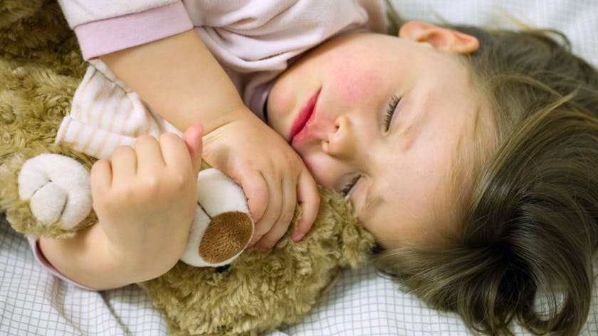 Ein Mädchen schläft mit ihrem Teddy im Arm.&nbsp;