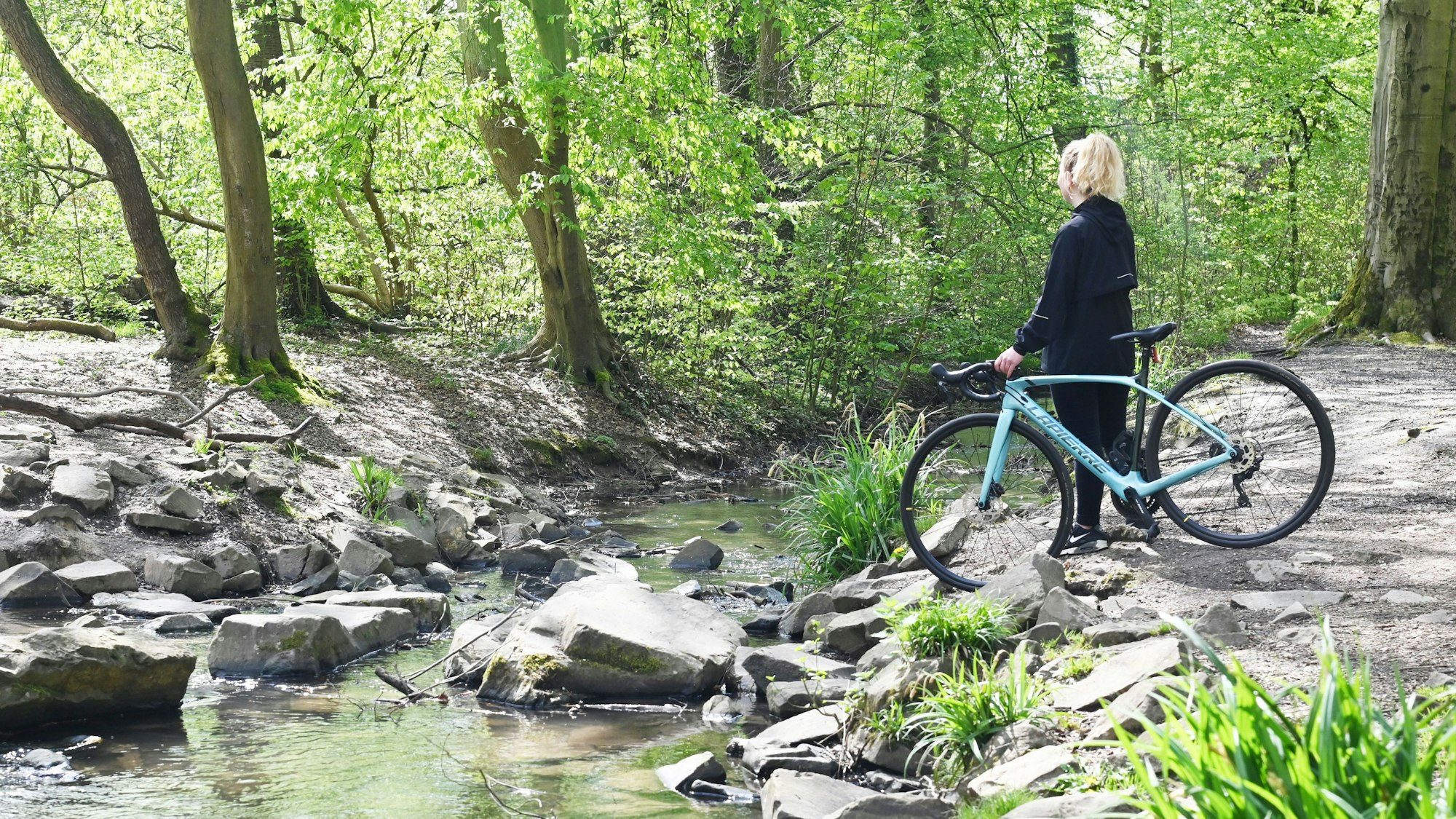 Radfahrerin steht am Wasser des Strundradwegs im rechtsrheinischen Köln
