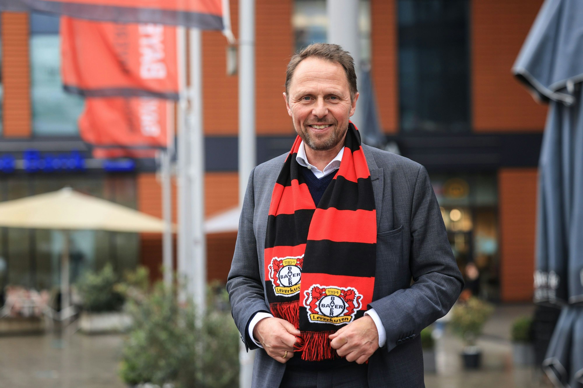 Uwe Richrath, Oberbürgermeister von Leverkusen, steht mit einem Fanschal vor dem Rathaus.