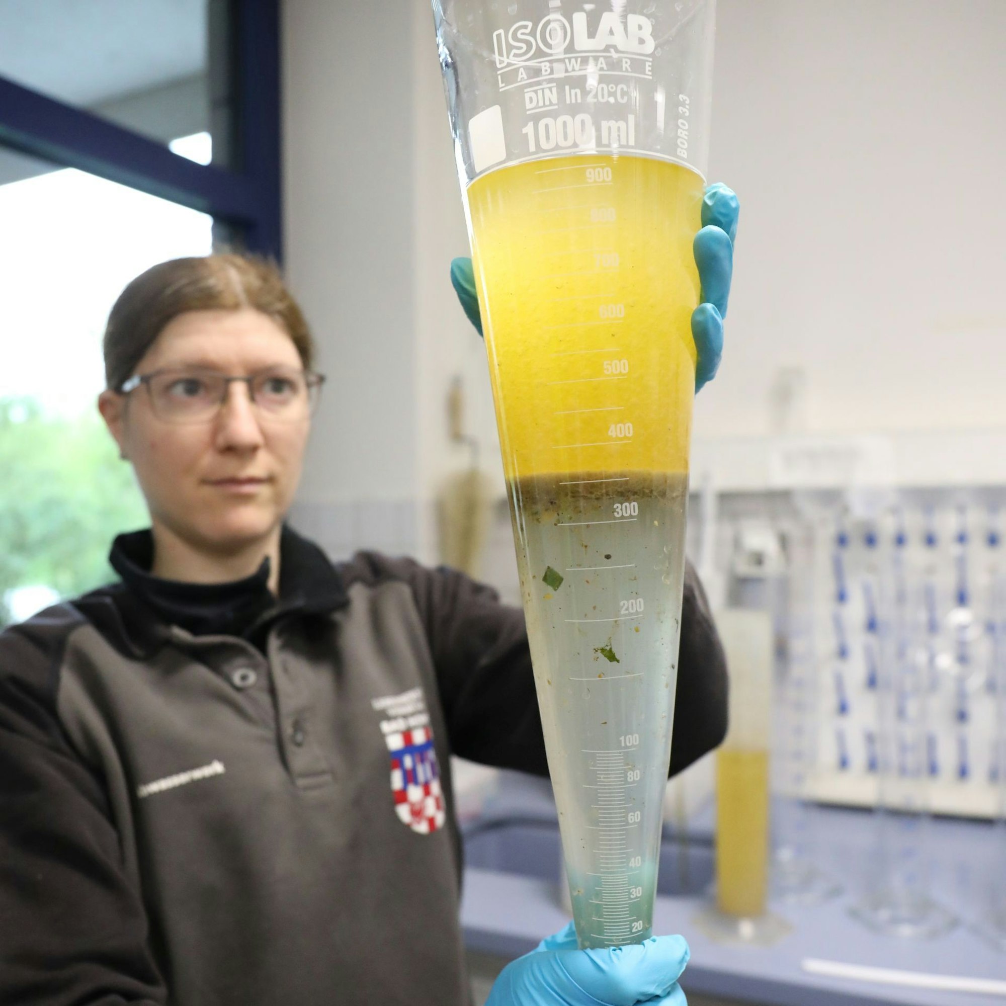 Eine Frau hält einen Glasbehälter mit einer weißlichen und gelben Flüssigkeit hoch.