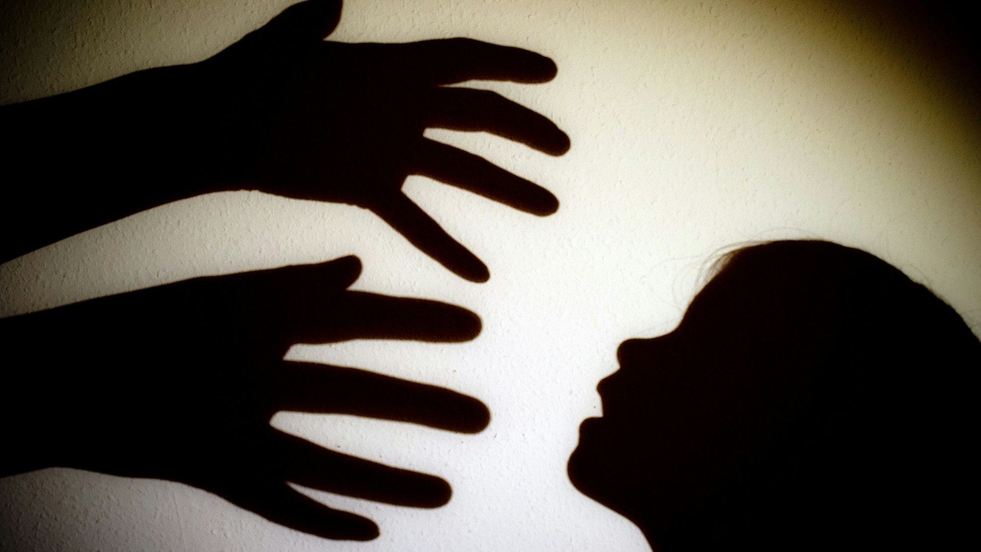 Schatten von Händen einer erwachsenen Person und dem Kopf eines Kindes an einer Wand eines Zimmers.