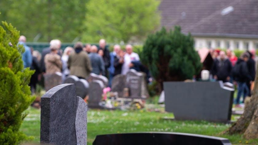 Trauergäste stehen auf einem Friedhof.