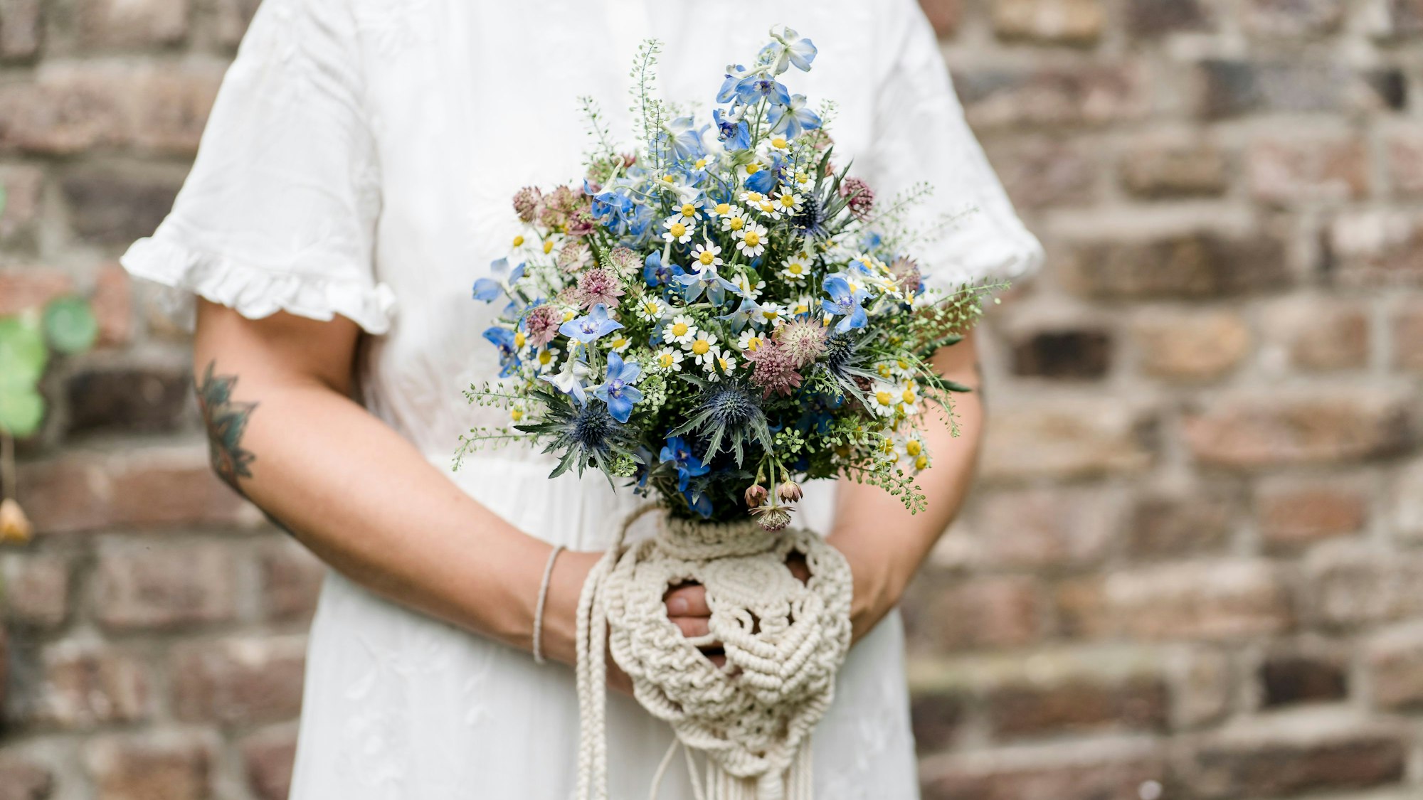 Eine Braut trägt ein Secondhand-Hochzeitskleid, der Brautstrauß besteht aus regionalen Wiesenblumen.