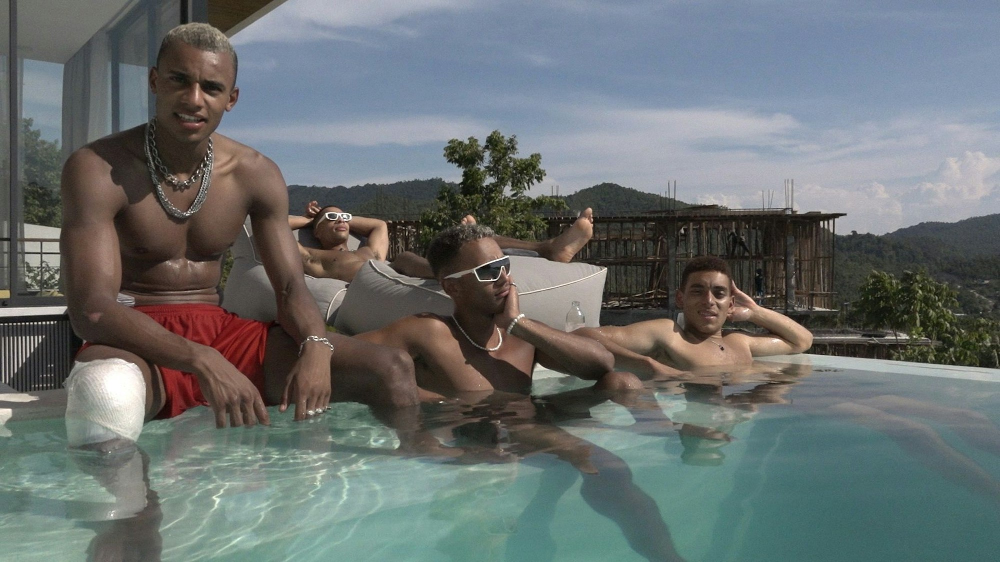Vier junge Männer posieren und lümmeln am Pool.
