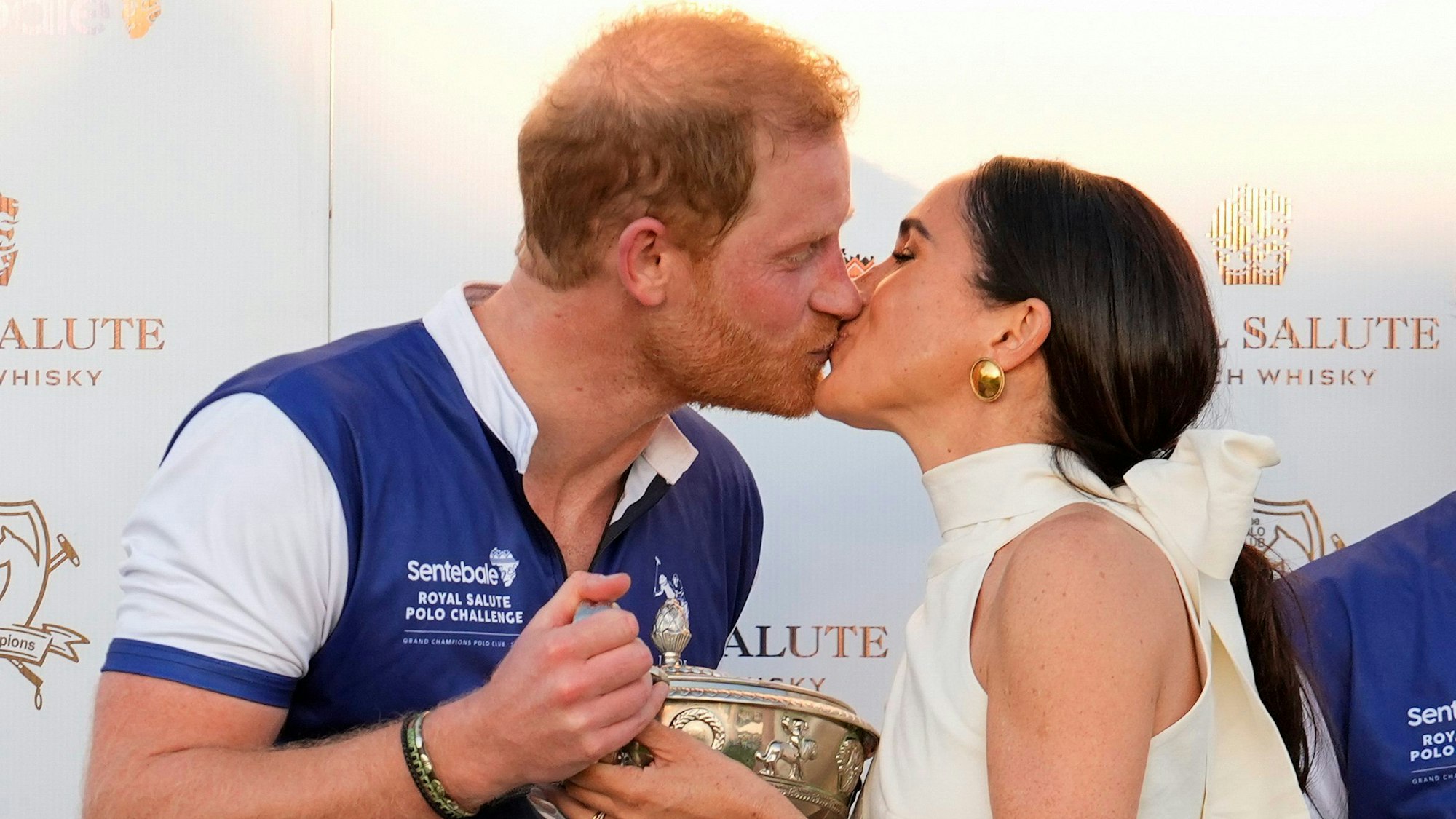 Der britische Prinz Harry (l), und seine Frau Meghan küssen sich, während sie seinem Polo-Team die Trophäe für den Sieg bei der Royal Salute Polo Challenge to Benefit Sentebale überreicht.