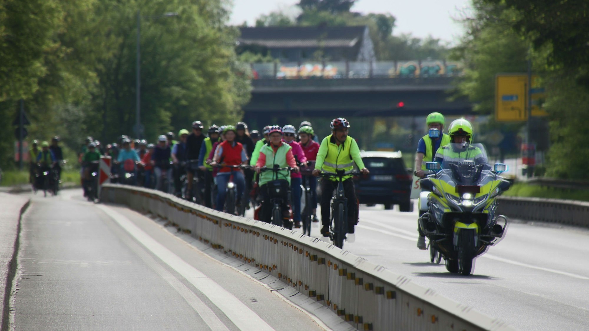 Ein dichter Pulk von Fahrradfahrern, begleitet von Polizei auf einem Motorrad.