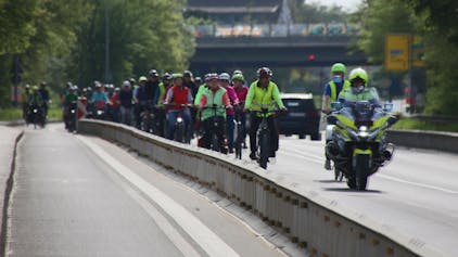 Ein dichter Pulk von Fahrradfahrern, begleitet von Polizei auf einem Motorrad.&nbsp;