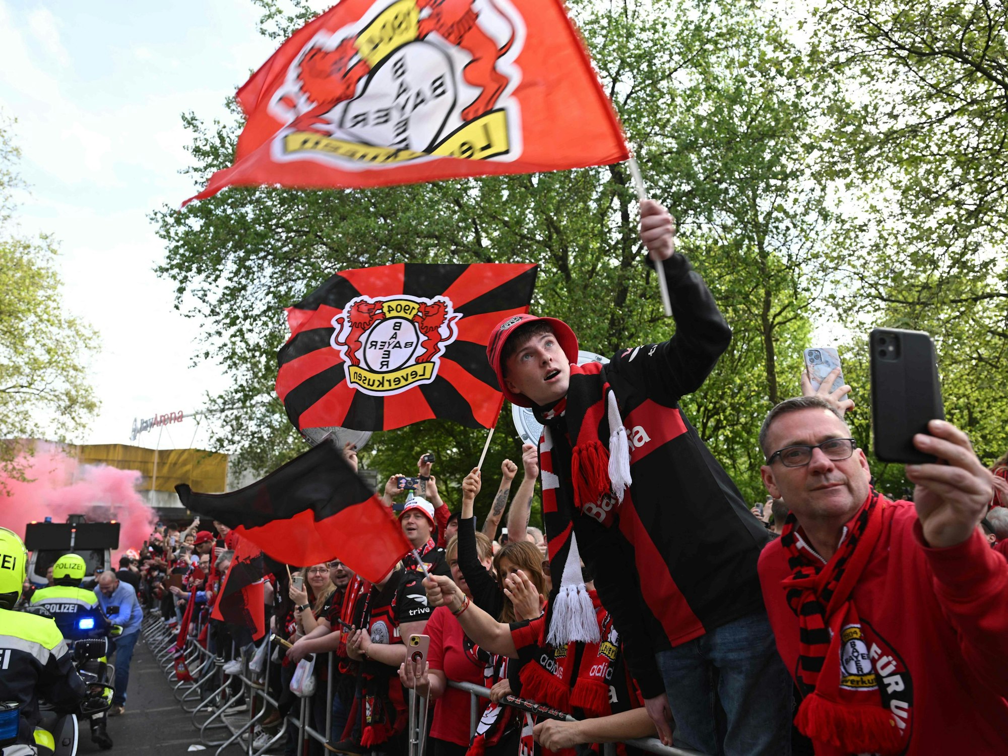 Leverkusen-Fans schwenken auf der Straße Fahnen und Filmen.