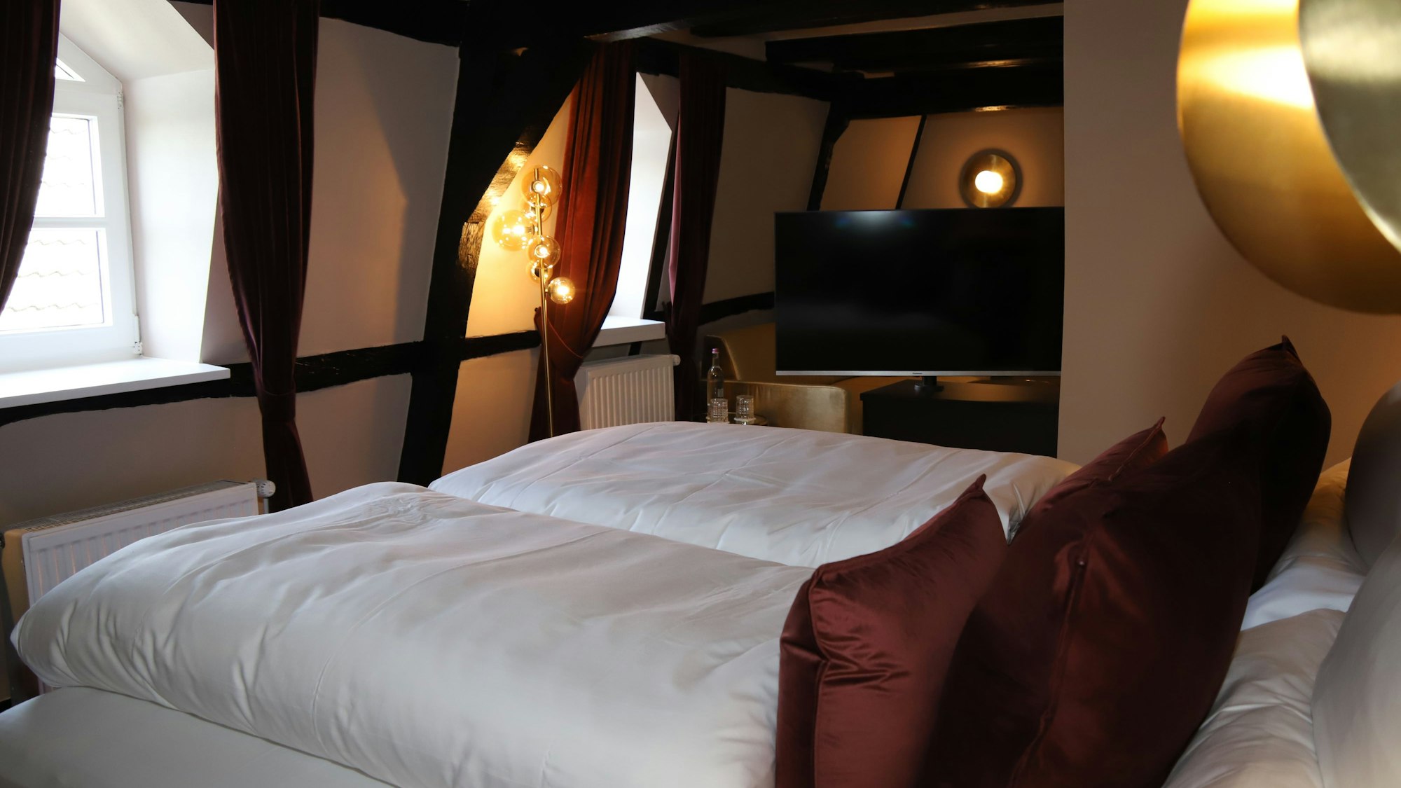 In einem Fachwerkzimmer steht ein Doppelbett mit dicken, weißen Plumeaus und dunklen Kissen.