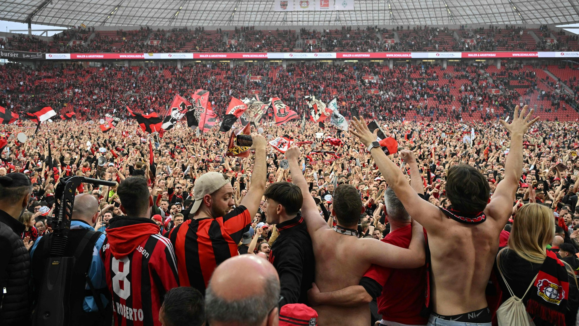 Leverkusen fans celebrate on the pitch after the German first division Bundesliga football match Bayer 04 Leverkusen v Werder Bremen in Leverkusen, western Germany, on April 14, 2024. Bayer Leverkusen were crowned 2023-24 Bundesliga champions for the first time on April 14, 2024.  (Photo by INA FASSBENDER / AFP) / DFL REGULATIONS PROHIBIT ANY USE OF PHOTOGRAPHS AS IMAGE SEQUENCES AND/OR QUASI-VIDEO