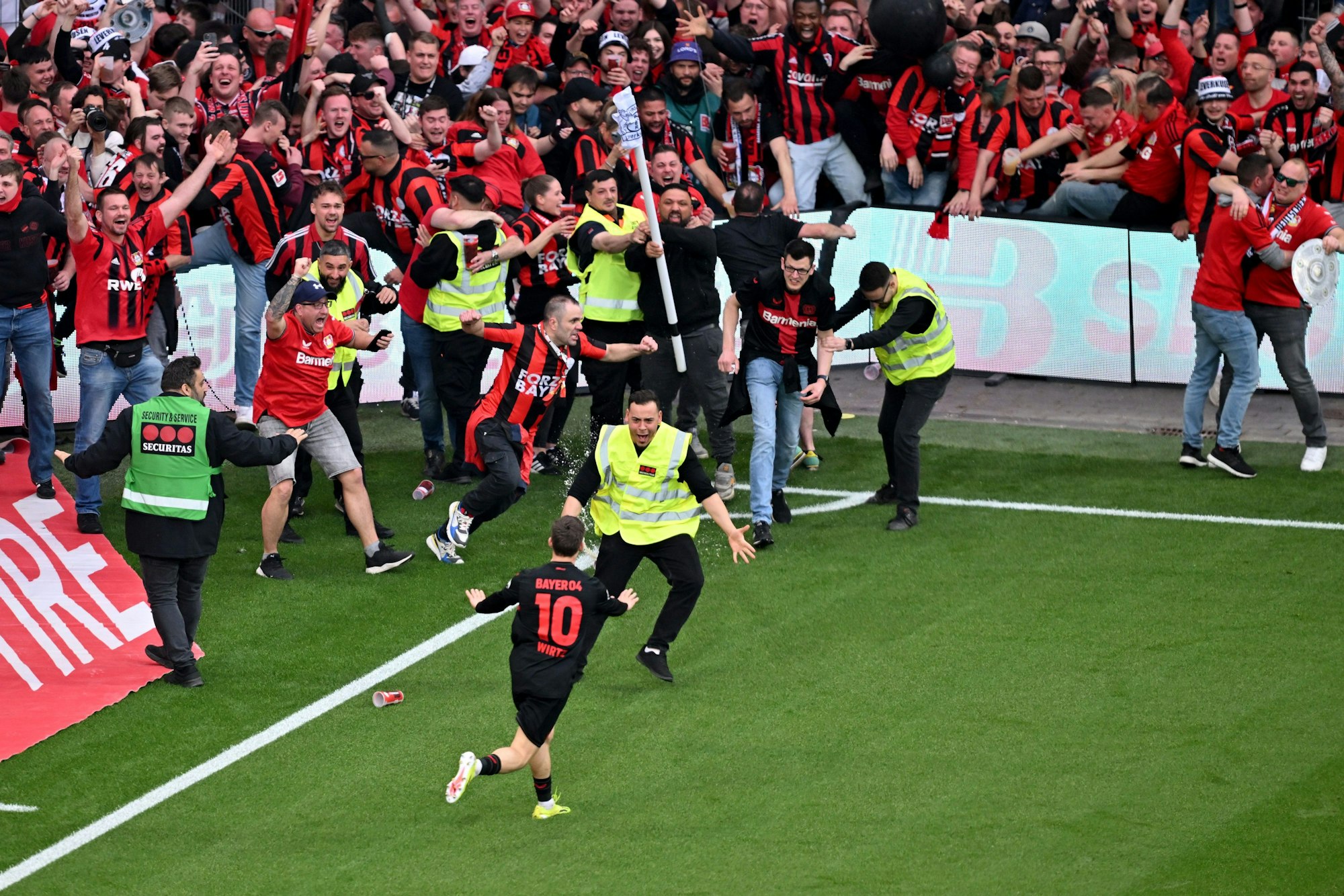 Leverkusens Florian Wirtz (vorne M, #10) dreht nach seinem Tor zum 4:0 jubelnd ab und beruhigt Fans und Sicherheitspersonal, die auf das Spielfeld laufen.