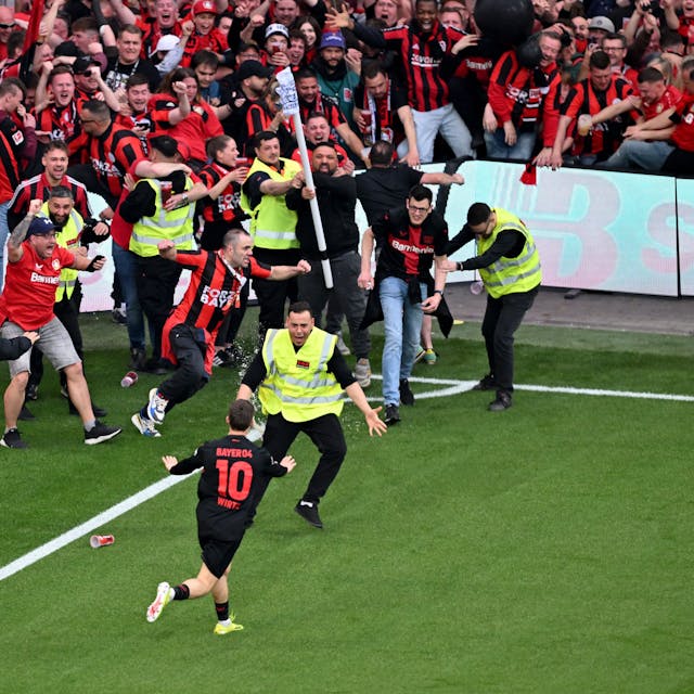 Leverkusens Florian Wirtz dreht nach seinem Tor zum 4:0 jubelnd ab und beruhigt Fans und Sicherheitspersonal, die auf das Spielfeld laufen.