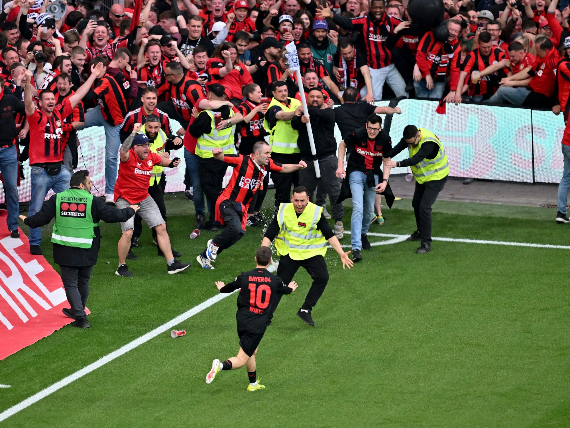 Leverkusens Florian Wirtz dreht nach seinem Tor zum 4:0 jubelnd ab und beruhigt Fans und Sicherheitspersonal, die auf das Spielfeld laufen.
