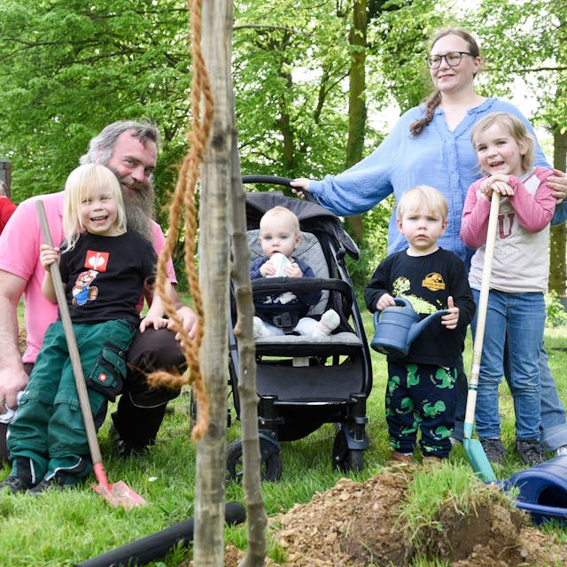 Eine Familie mit vier Kindern pflanzt einen Baum.