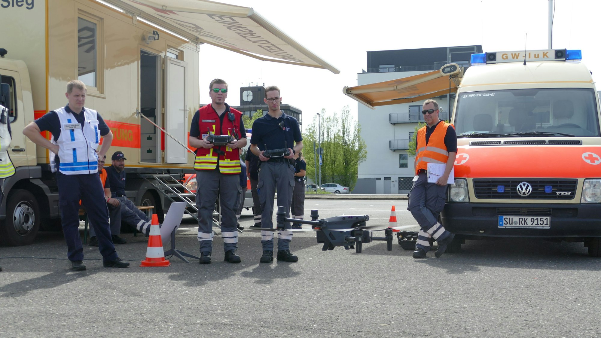 Mehrere Männer in Einsatzkleidung stehen vor einer Drohne, die einer von ihnen per Fernsteuerung bedient.