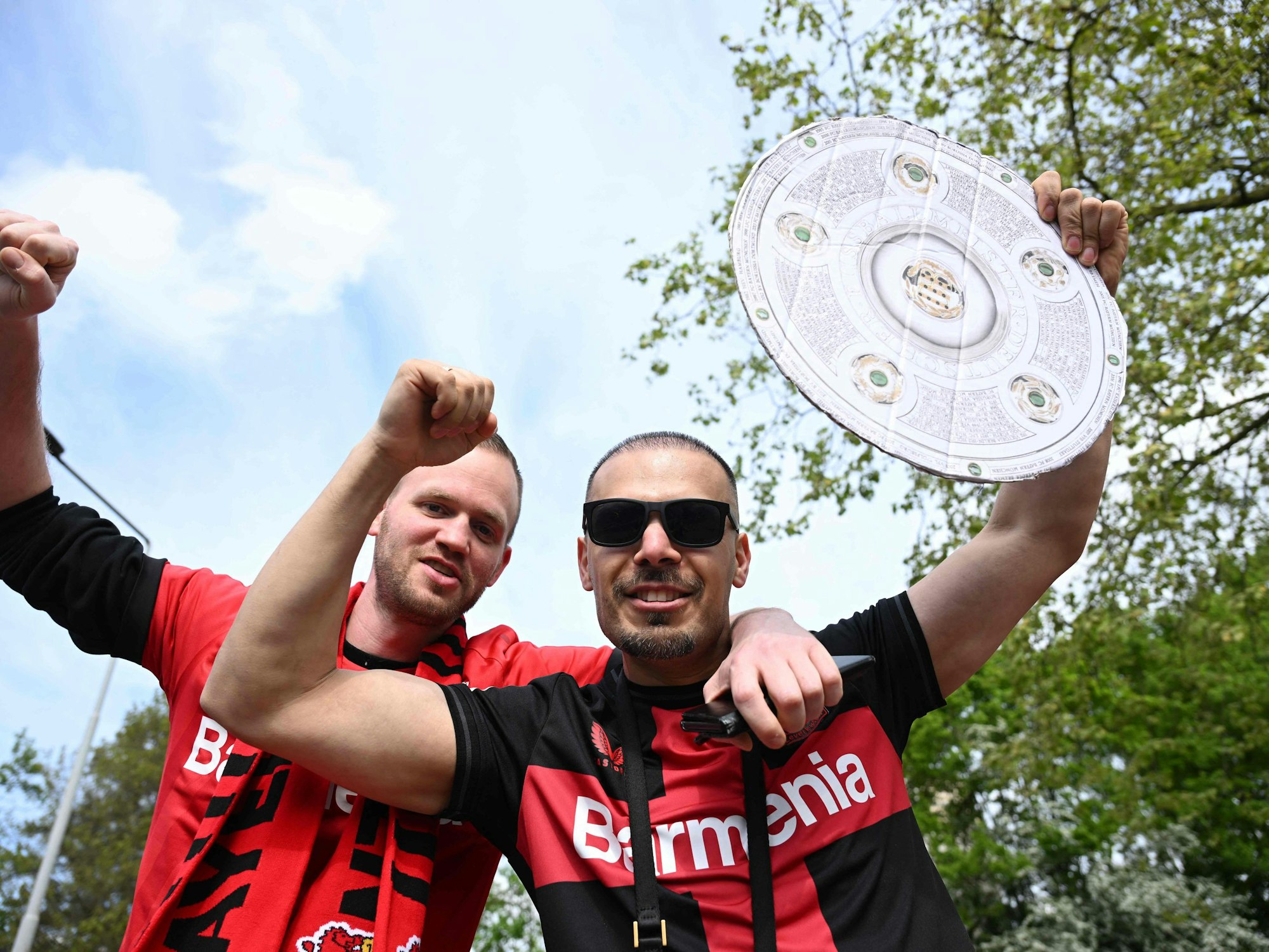 Zwei Leverkusen-Fans halten eine Meisterschale aus Pappe hoch.