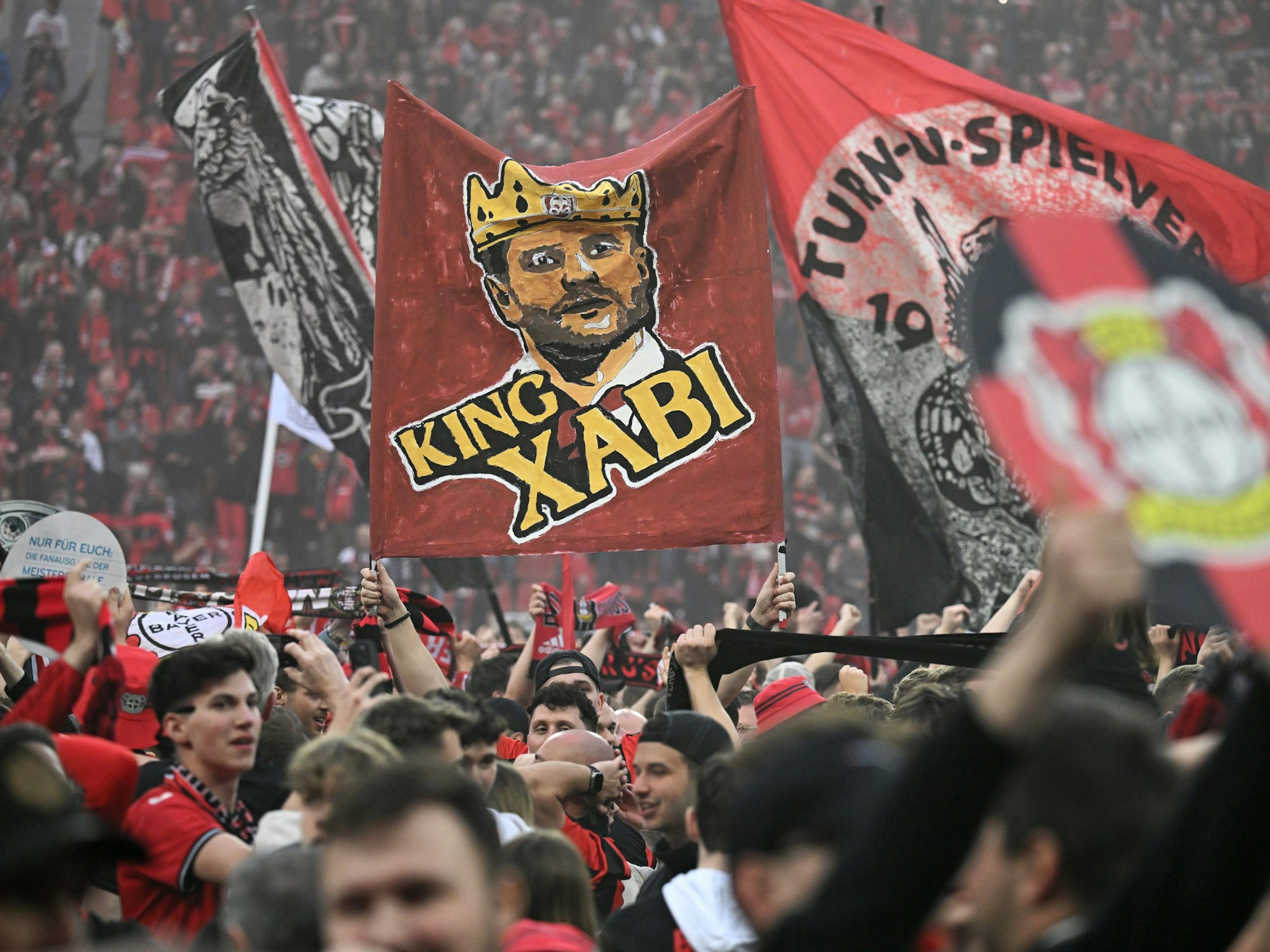 Leverkusener Fans haben nach dem Sieg ihrer Mannschaft das Spielfeld gestürmt und halten eine Fahne mit der Aufschrift "King Xabi" für Leverkusens Trainer Xabi Alonso.