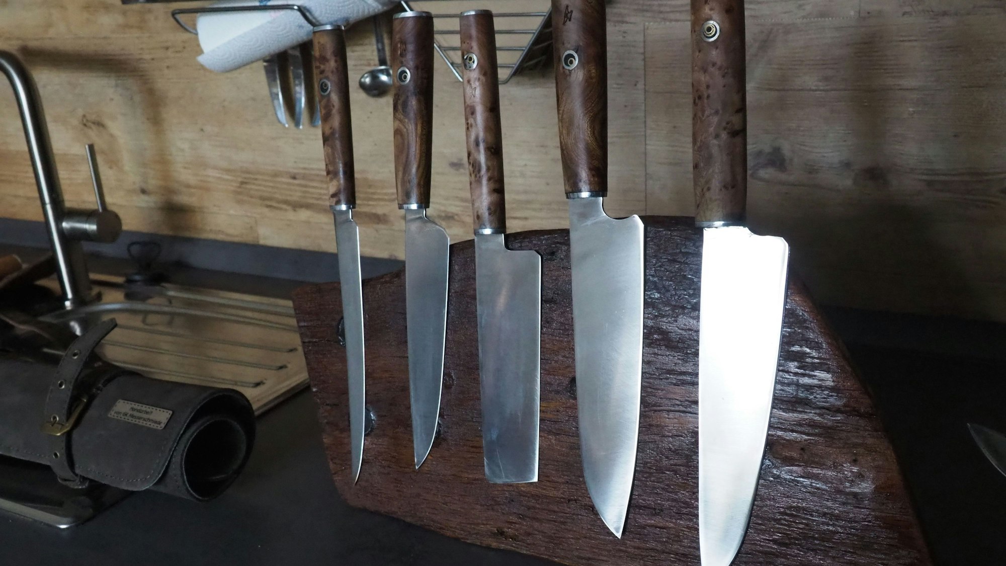 Das Bild zeigt fünf Messer, die an einem alten Holzstück haften.