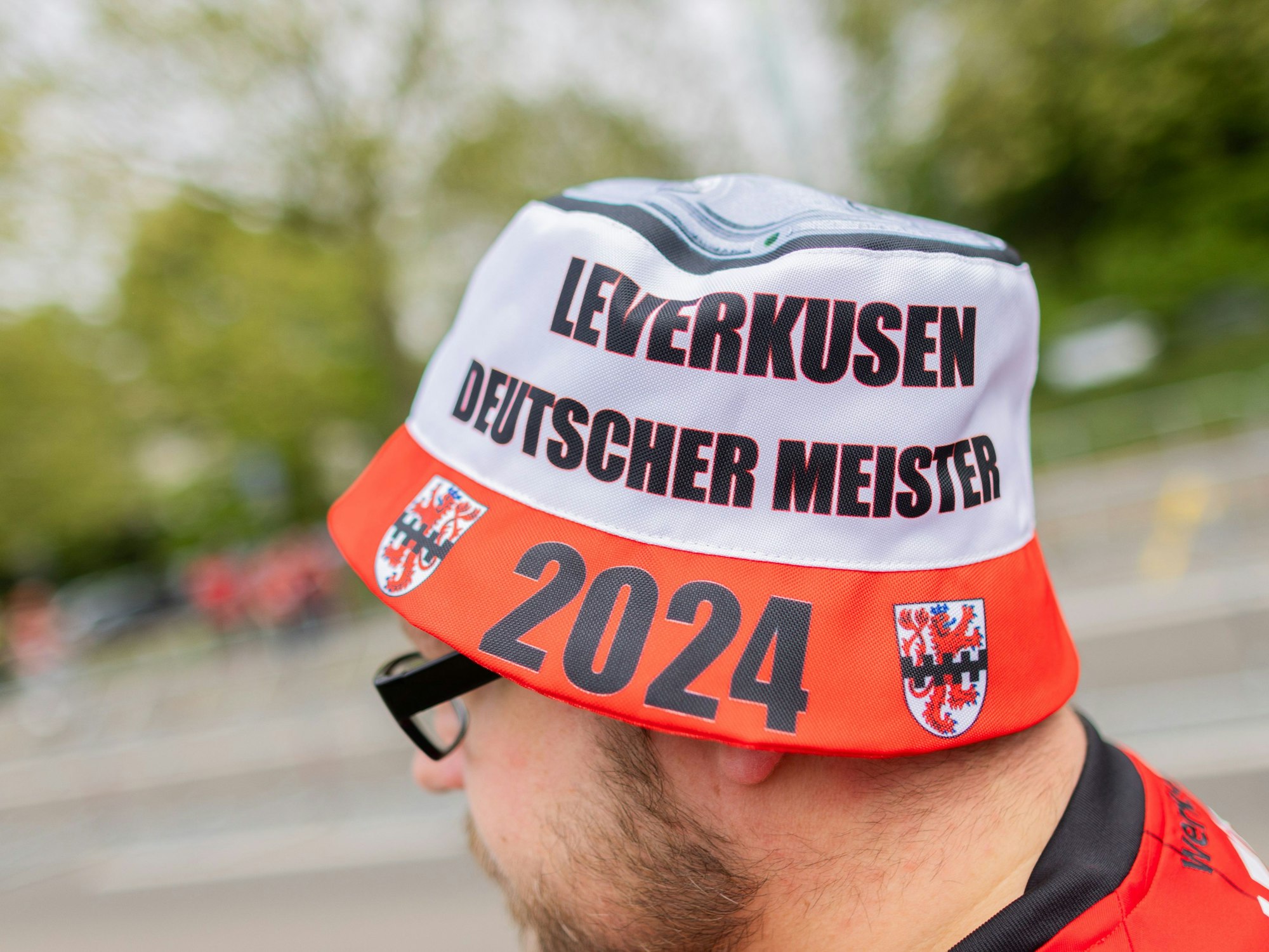 Ein Fan trägt eine Mütze mit der Aufschrift ·Leverkusen - Deutscher Meister 2024· und einer stilisierten Meisterschale.