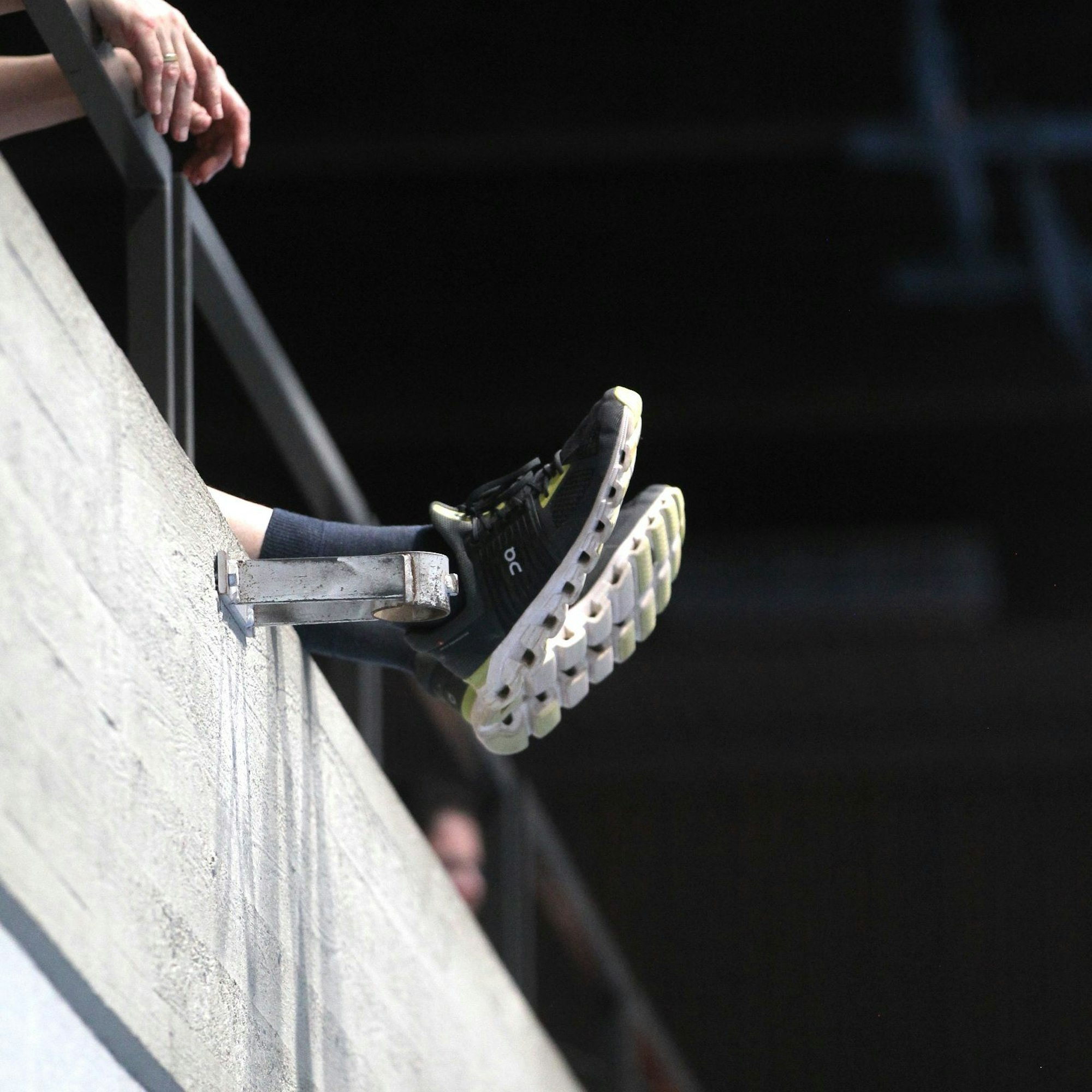 Füße eines Zuschauers auf der Tribüne hängen über den Betonrand hinaus in der Luft.