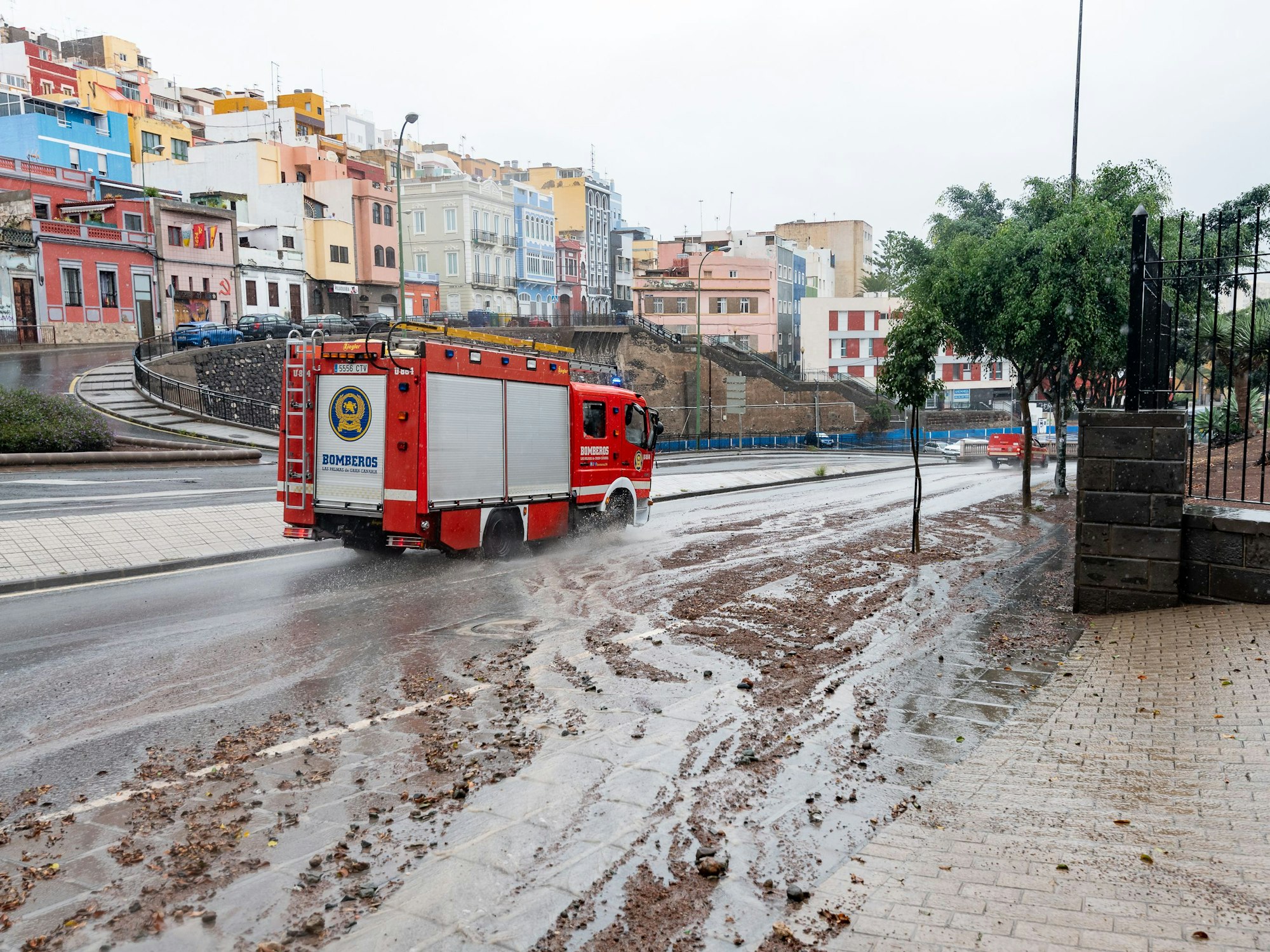Ein Feuerwehrauto fährt nach Regen eine schlammige Straße entlang.