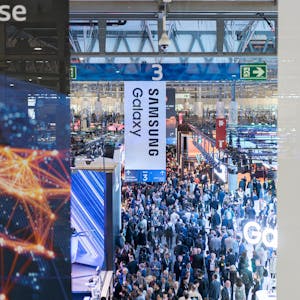 Besucher gehen durch die Messehalle auf der europäischen Mobilfunkmesse Mobile World Congress (MWC), im Vorgrund sind Schilder von Samsung Galaxy zu sehen.