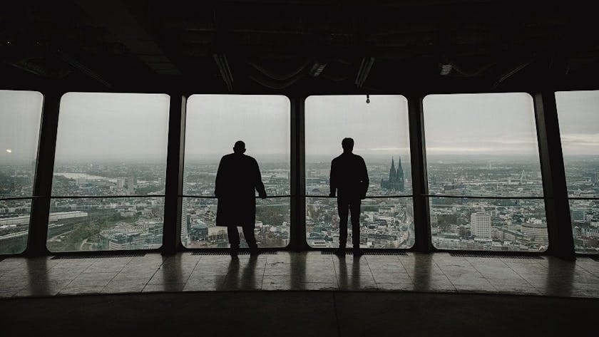 Zu sehen sind die „Tatort“-Kommissare Freddy Schenk und Max Ballauf in der Rückansicht, die vom „Colonius“ auf Köln blicken.