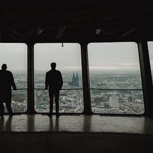 Zu sehen sind die „Tatort“-Kommissare Freddy Schenk und Max Ballauf in der Rückansicht, die vom „Colonius“ auf Köln blicken.