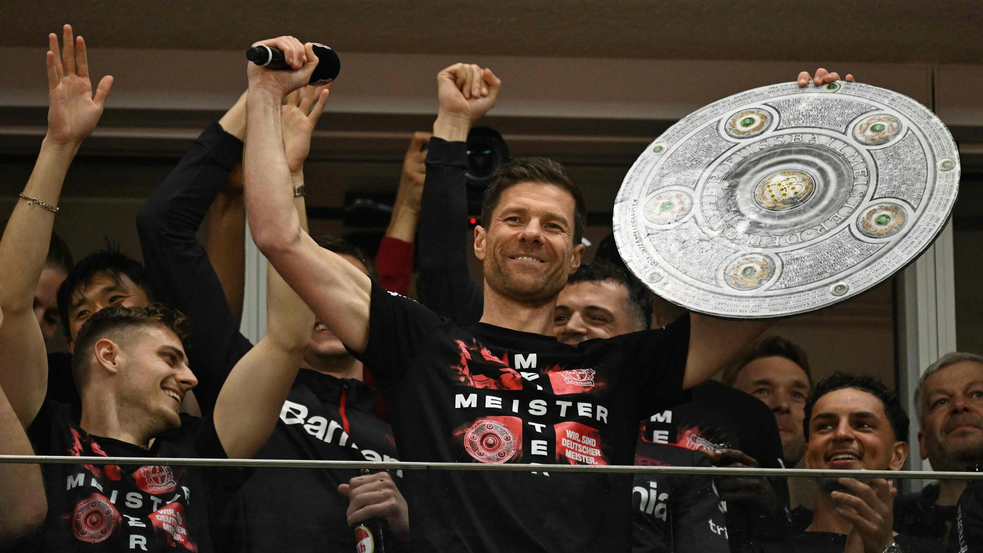 Xabi Alonso, Cheftrainer von Bayer Leverkusen, feiert auf der Tribüne mit einer Meisterschale aus Pappe.