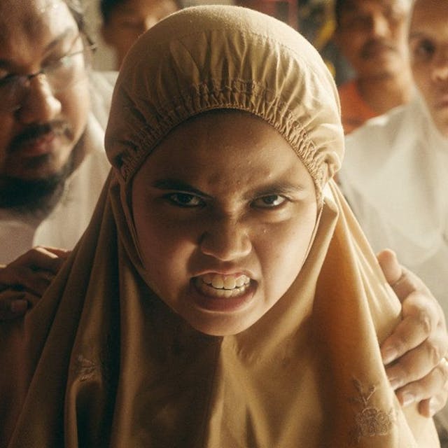 Die zwölfjährige Malaysierin Zaffan, die Hauptfigur im Film „Tiger Stripes“, blickt zornig und voller Wut. Im Hintergrund versuchen mehrere Erwachsene, sie sanft zurückzuhalten.
