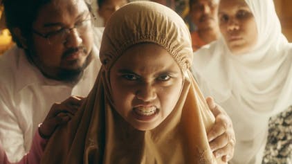 Die zwölfjährige Malaysierin Zaffan, die Hauptfigur im Film „Tiger Stripes“, blickt zornig und voller Wut. Im Hintergrund versuchen mehrere Erwachsene, sie sanft zurückzuhalten.