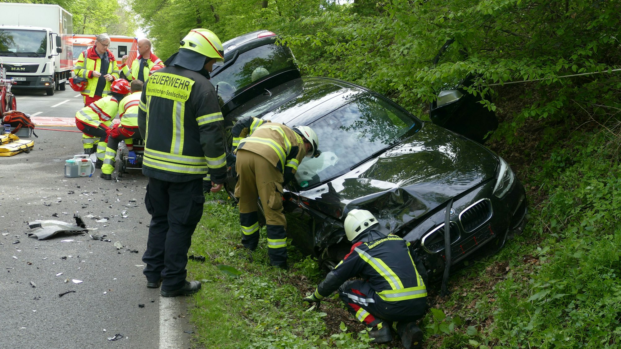 Feuerwehrleute untersuchen das Auto des Unfallverursachers, der dahinter verarztet wird.