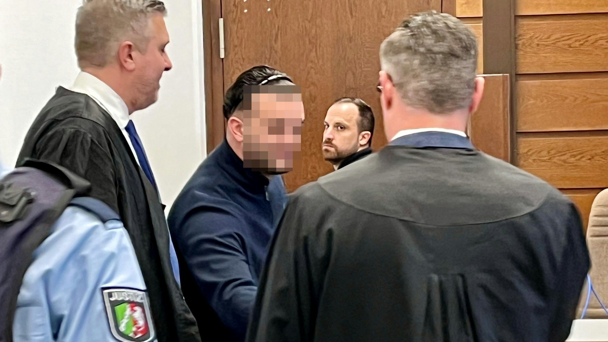 Ein Mann begrüßt im Gerichtssaal seine beiden Anwälte.