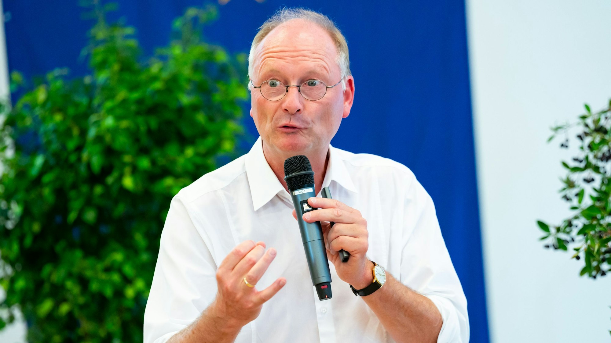 Wetterexperte und Meteorologe Sven Plöger hält bei einem Vortrag ein Mikrofon in der Hand. Er trägt ein weißes Hemd und eine Uhr.