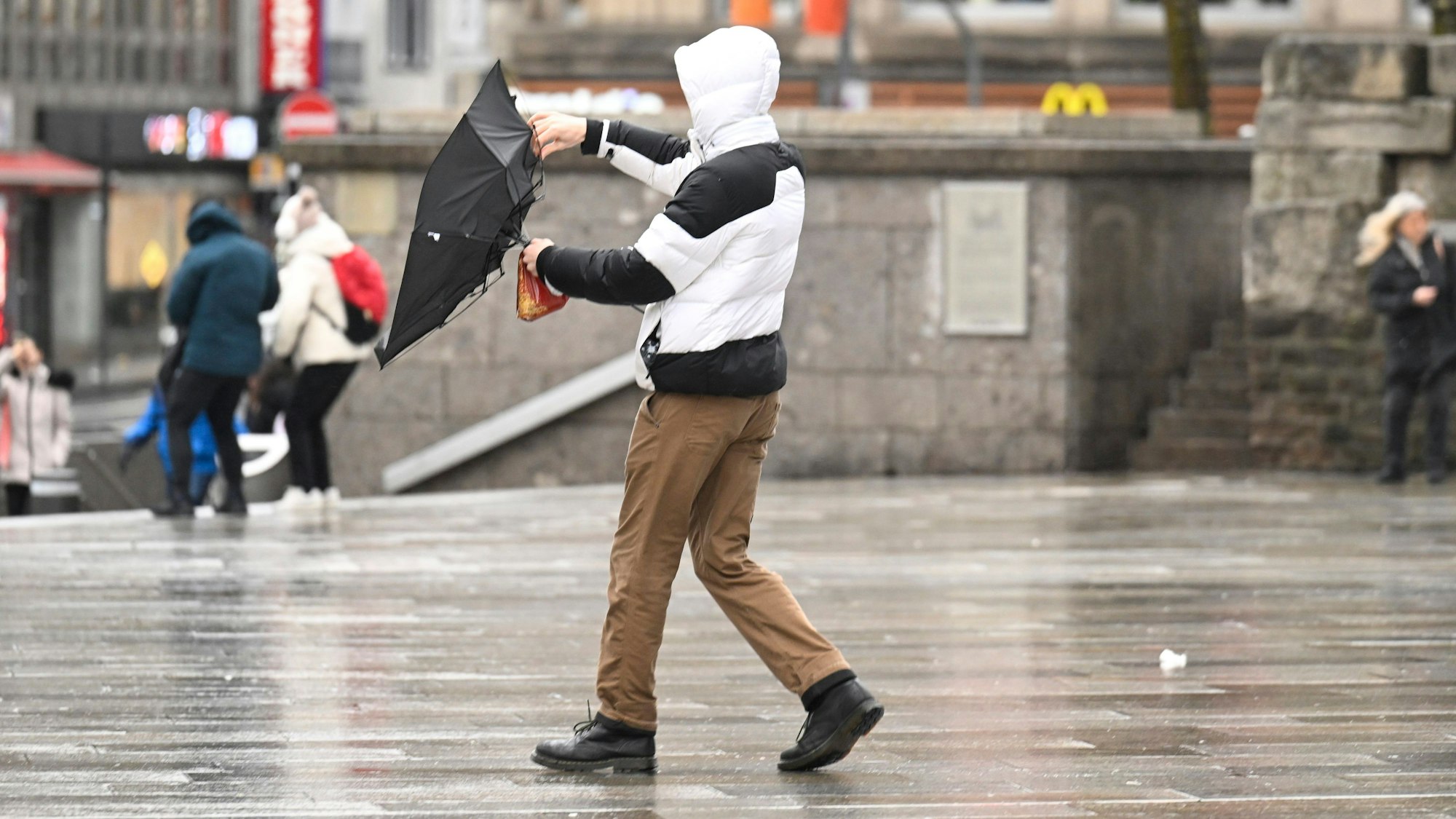 Ein Mann kämpft bei stürmischem Wetter in Köln mit seinem Regenschirm.
